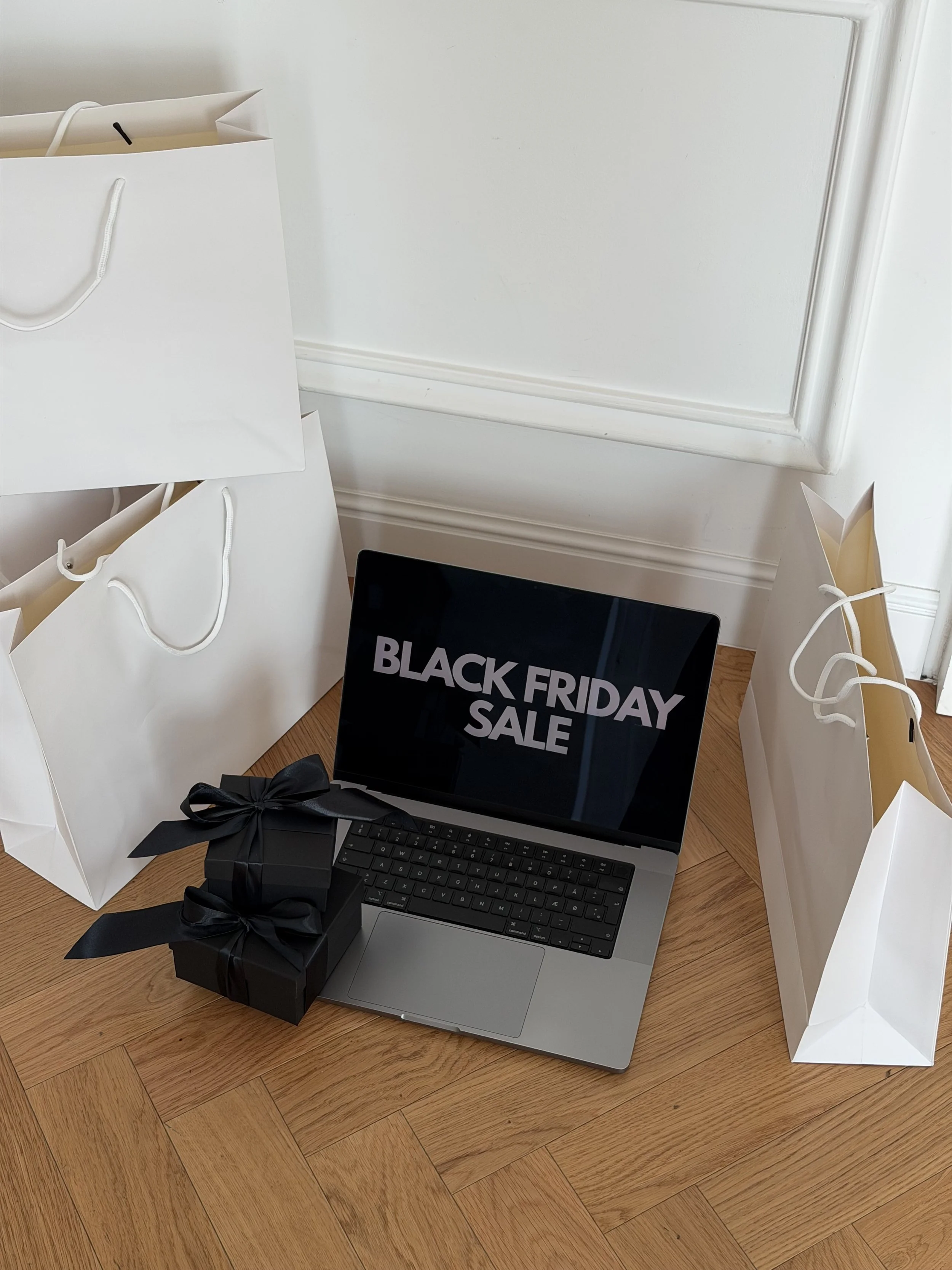 Black Friday sale on a laptop screen with a black gift box and white shopping bags in a corner