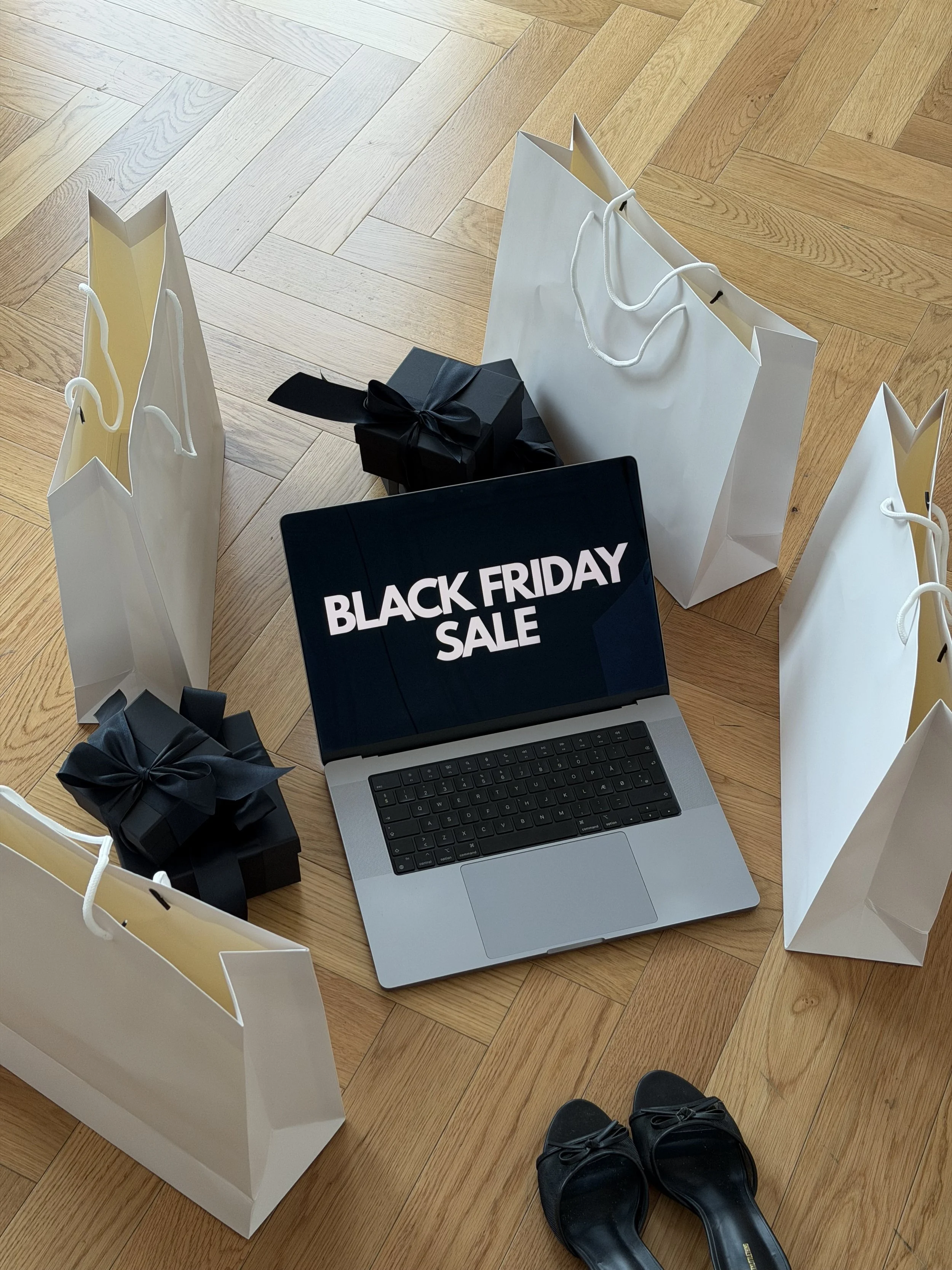 Laptop showing a Black Friday sale screen surrounded by shopping bags and gift boxes