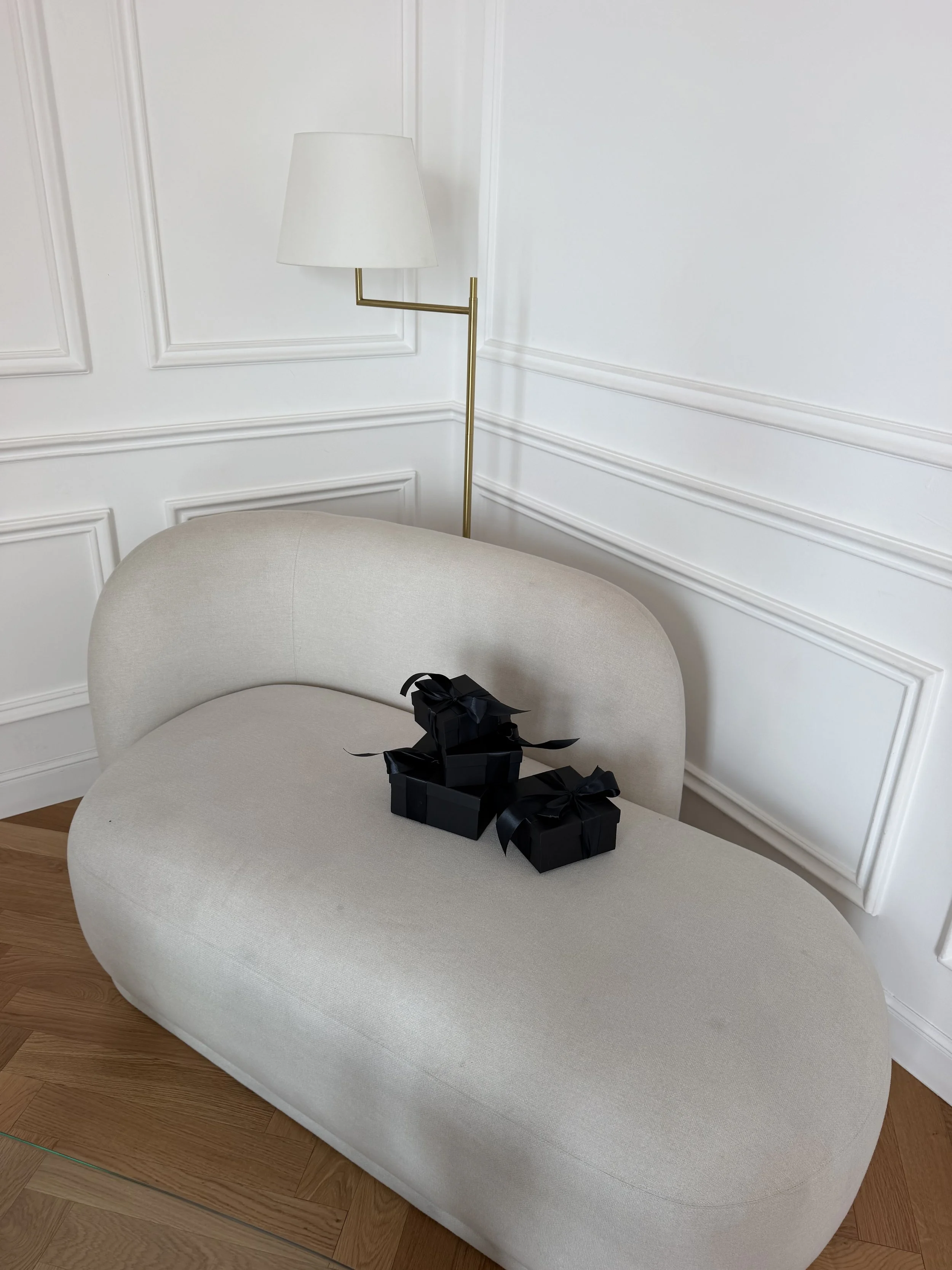 Black gift boxes with bows on a curved cream sofa in a bright Parisian-style room