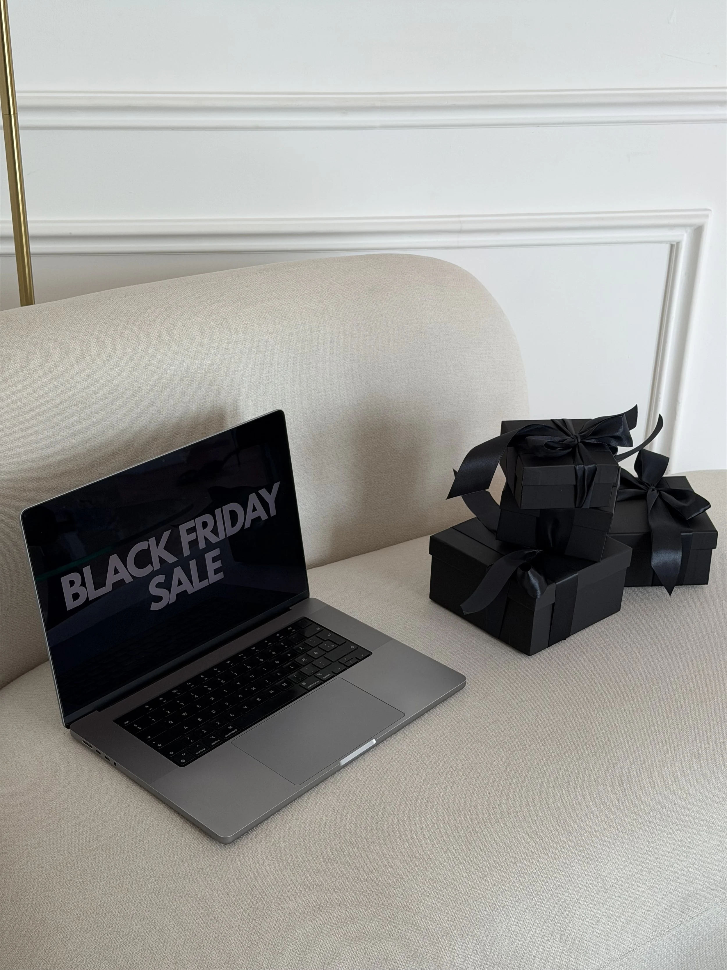 Laptop with Black Friday sale on screen next to black gift boxes on a sofa