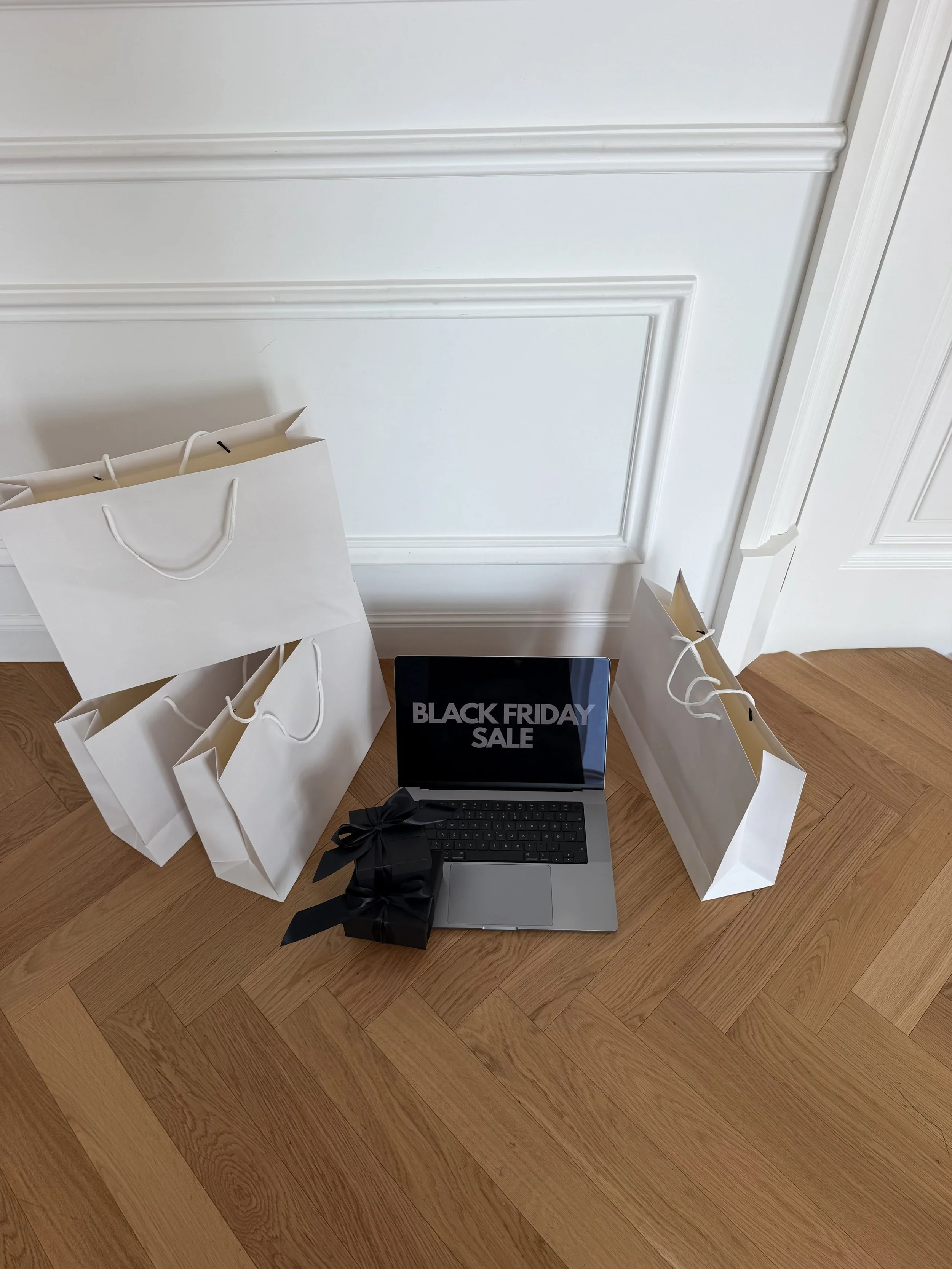 White shopping bags, black gift boxes and a laptop on a wooden floor for Black Friday