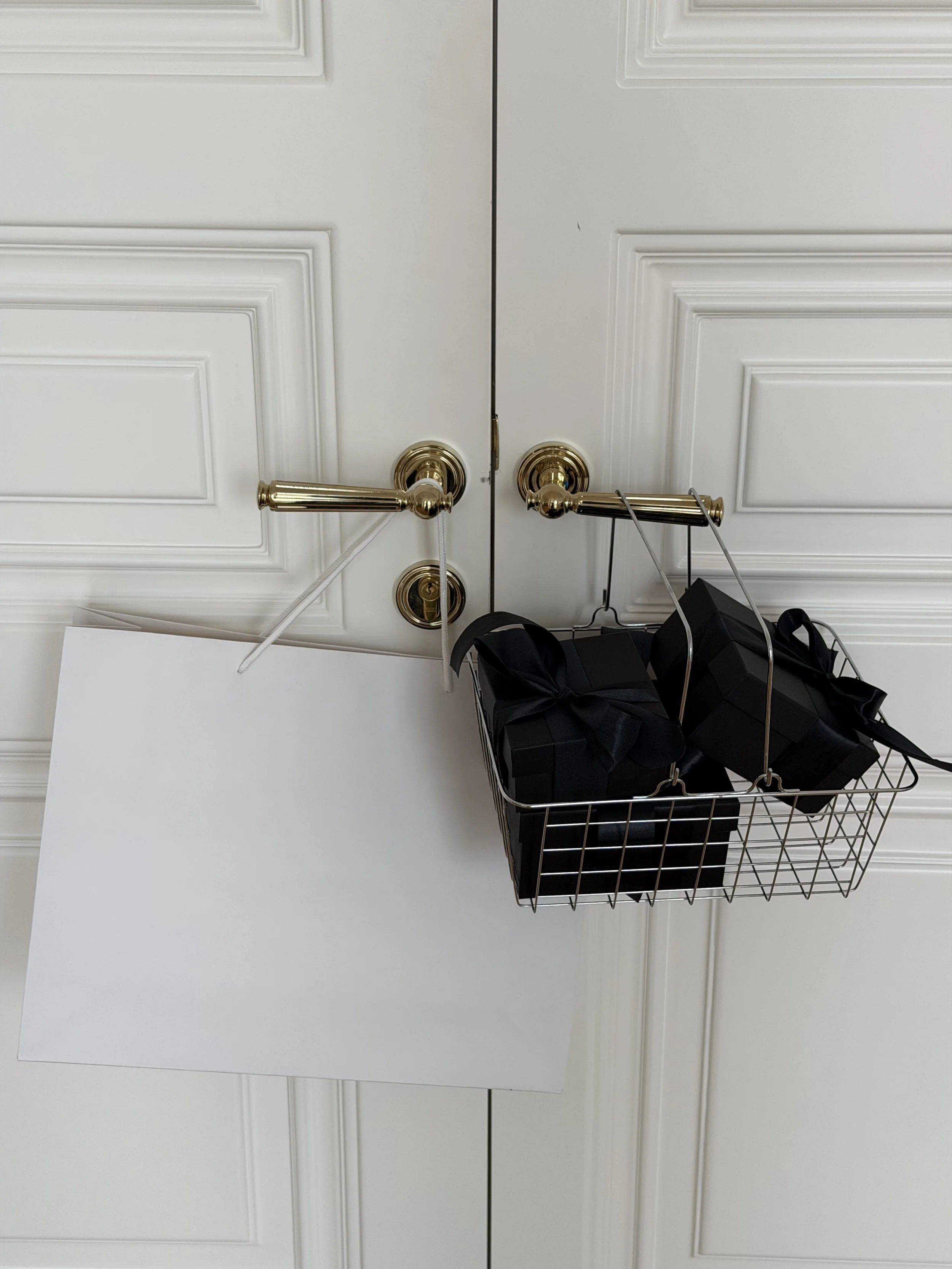 Blank white shopping bag mockup and basket of black gifts on gold door handles