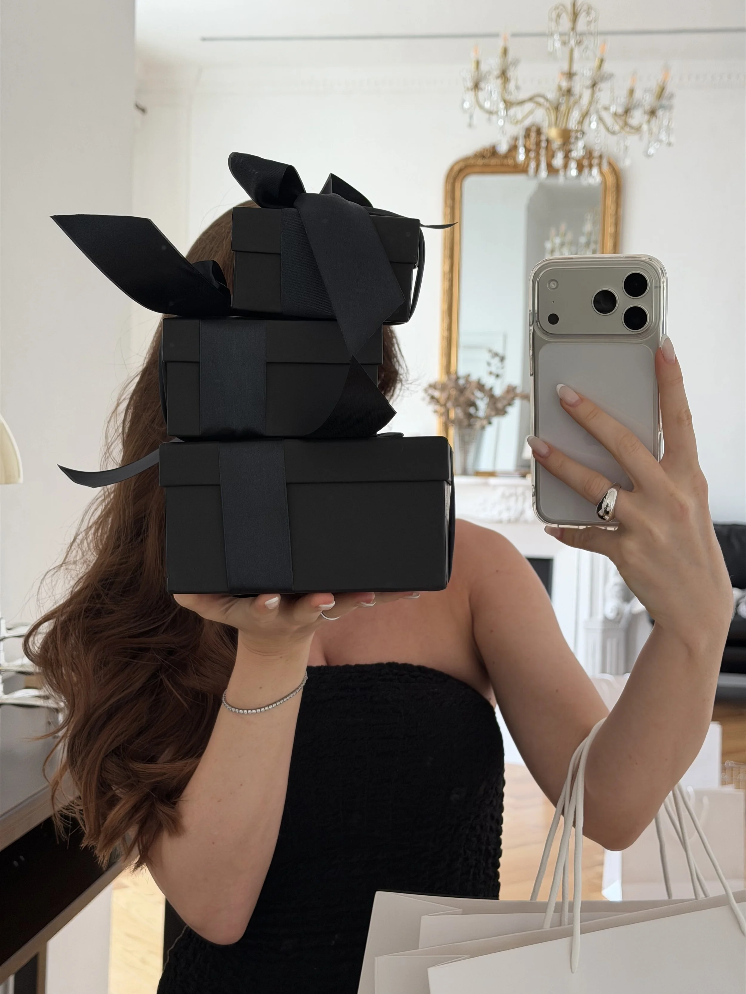 Mirror selfie of a woman carrying a tower of black Black Friday gift boxes
