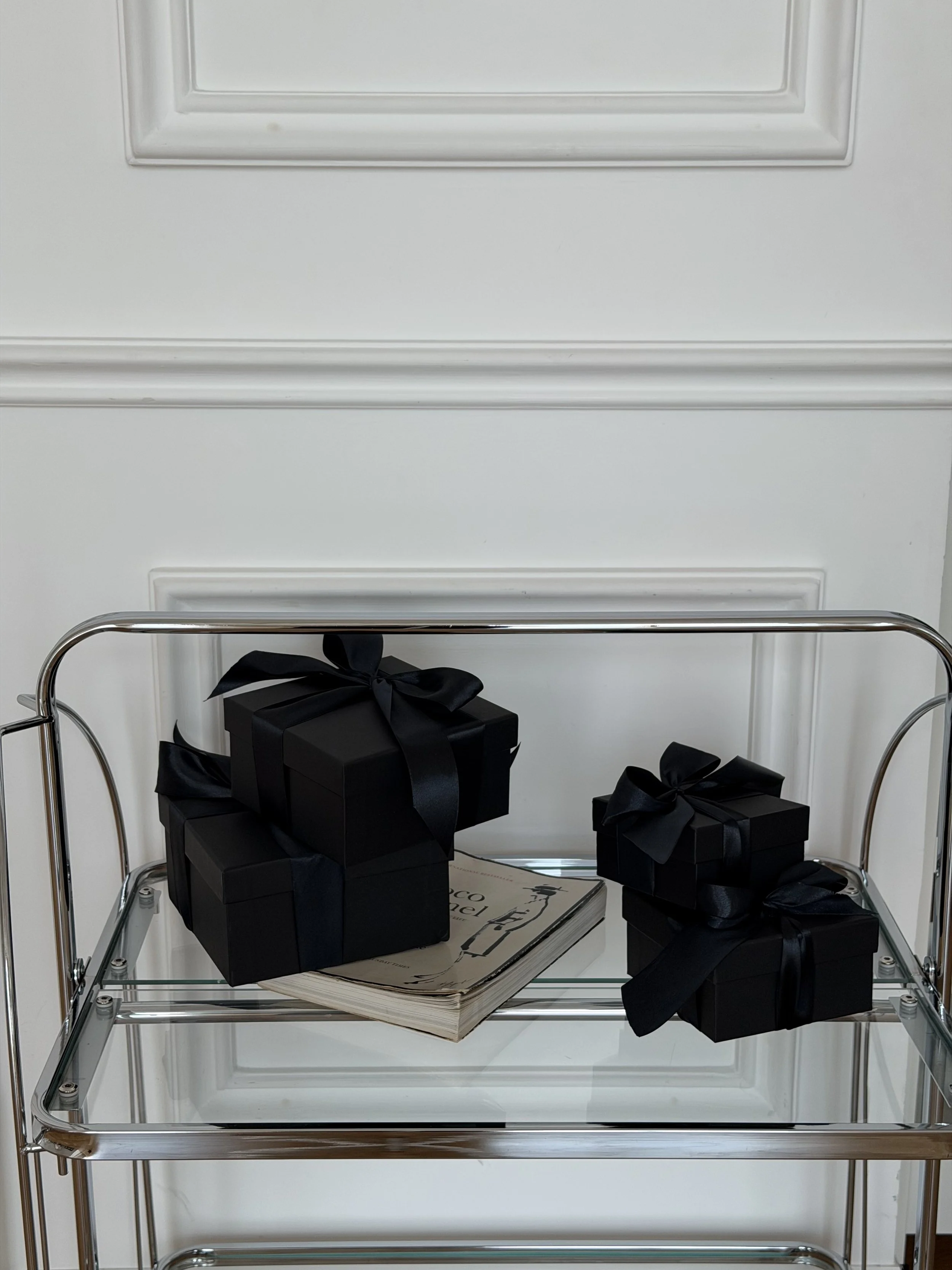 Black gift boxes on a chrome and glass bar cart in a white panelled room