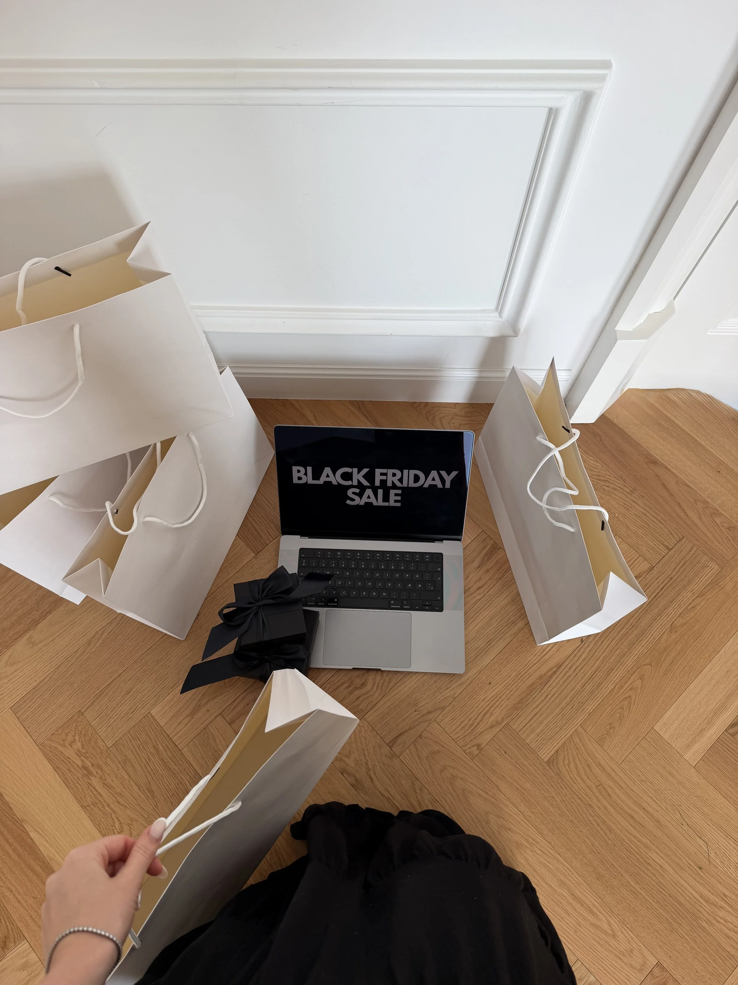 Top-down view of a laptop with a Black Friday sale screen among shopping bags on a herringbone floor
