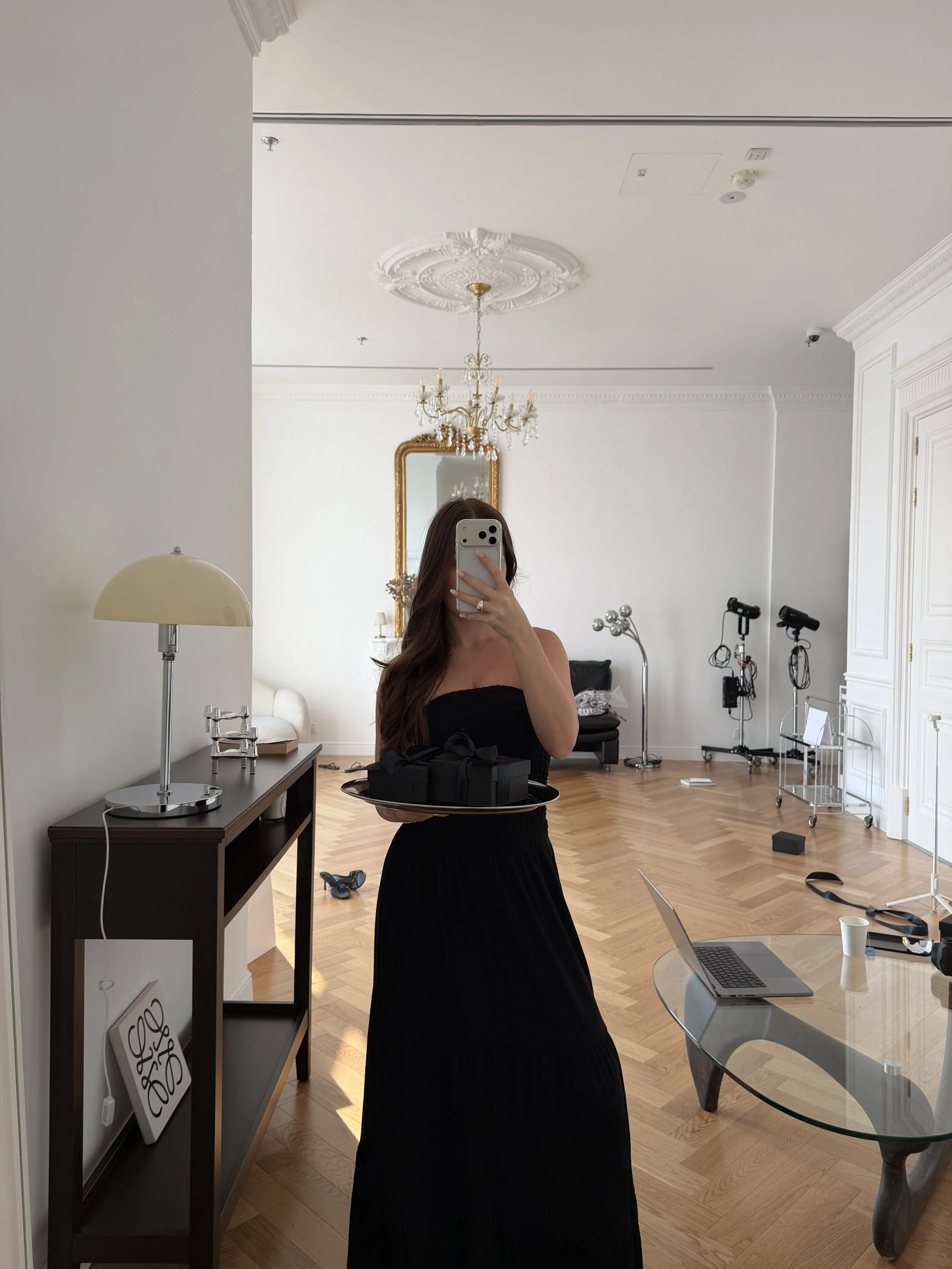Woman in a black dress holding gift boxes in an elegant apartment with chandelier