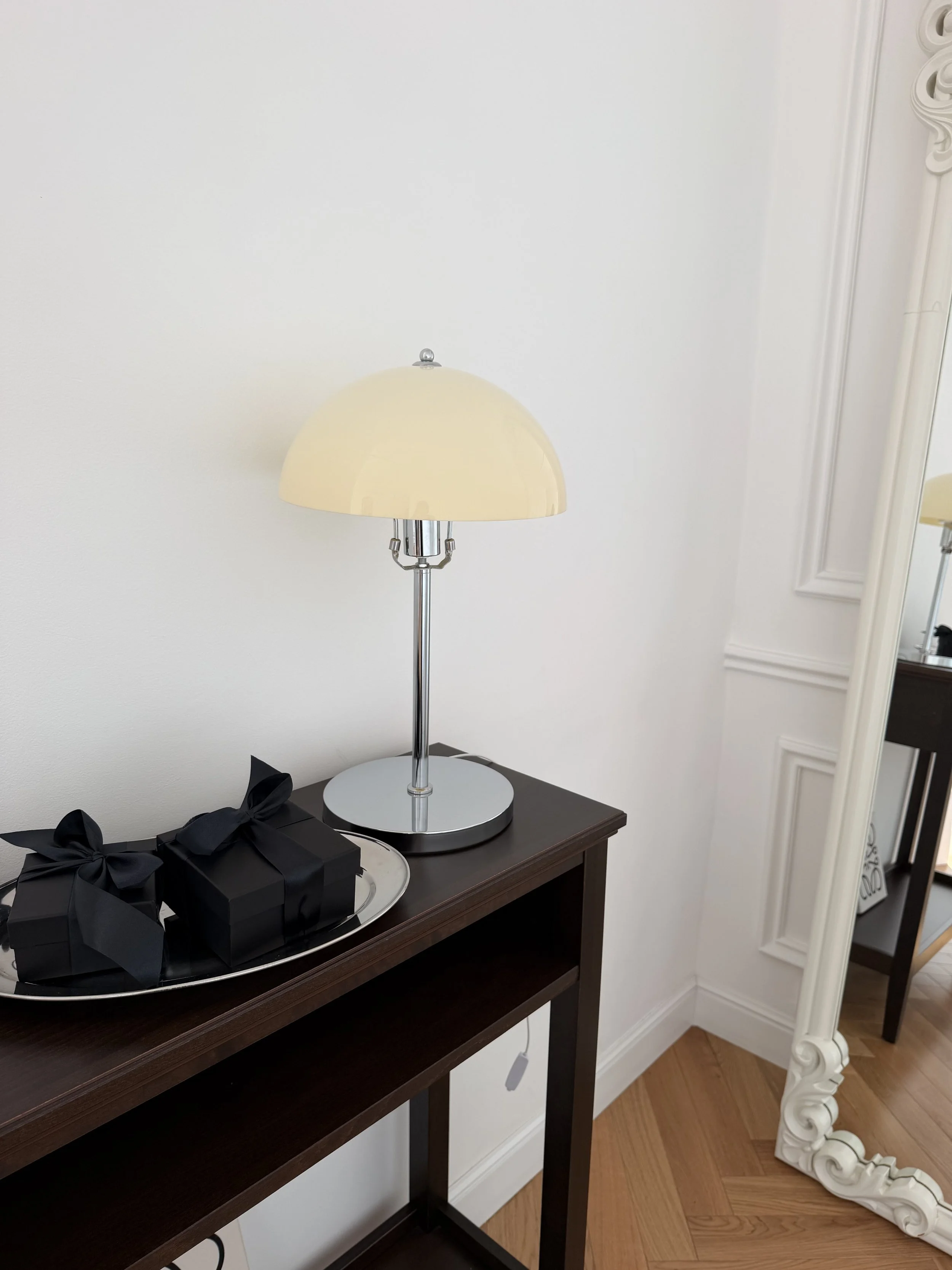Black gift boxes on a silver tray on a dark console table with a mushroom lamp