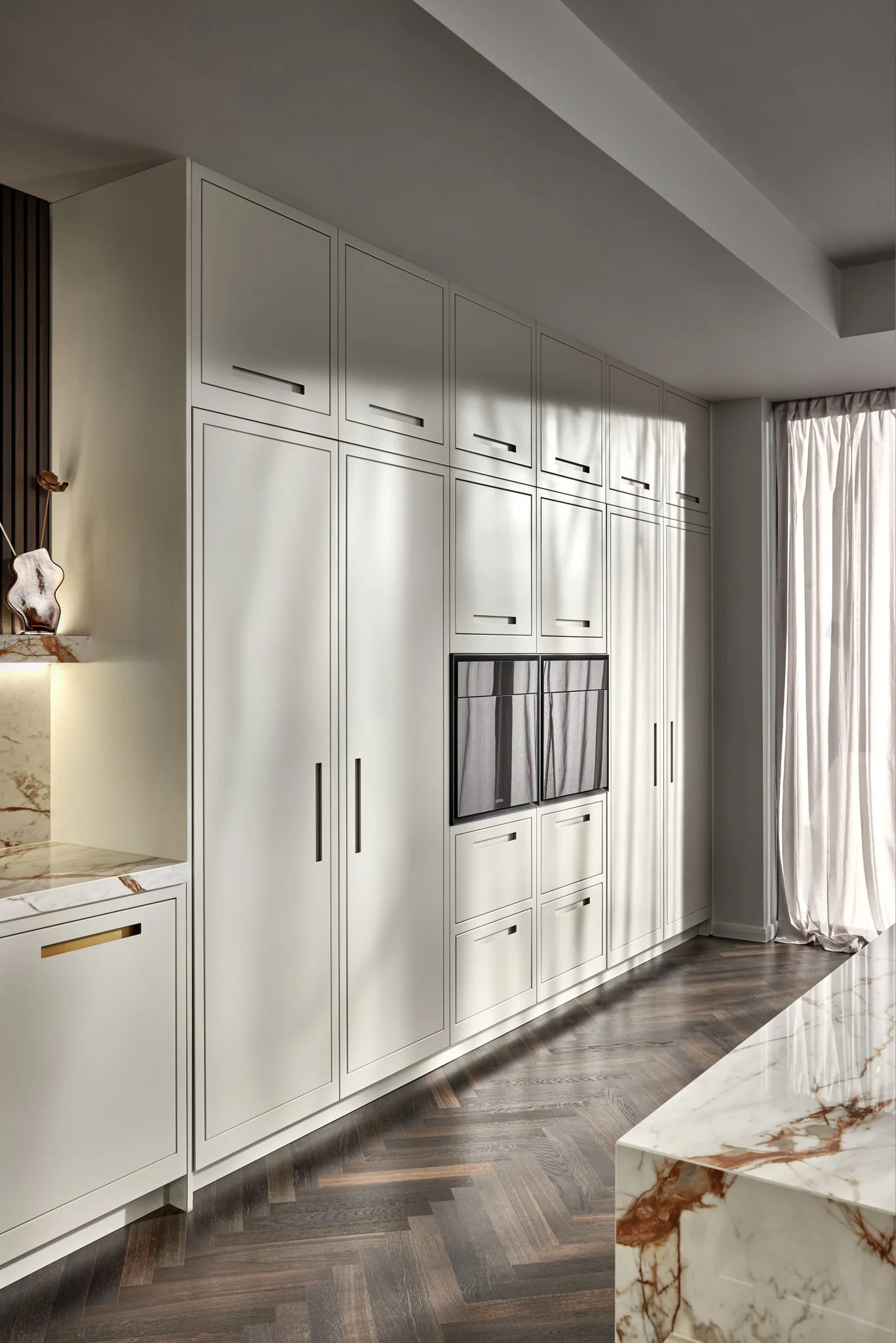 Modern kitchen interior with marble countertops, white cabinets, and herringbone wood flooring.