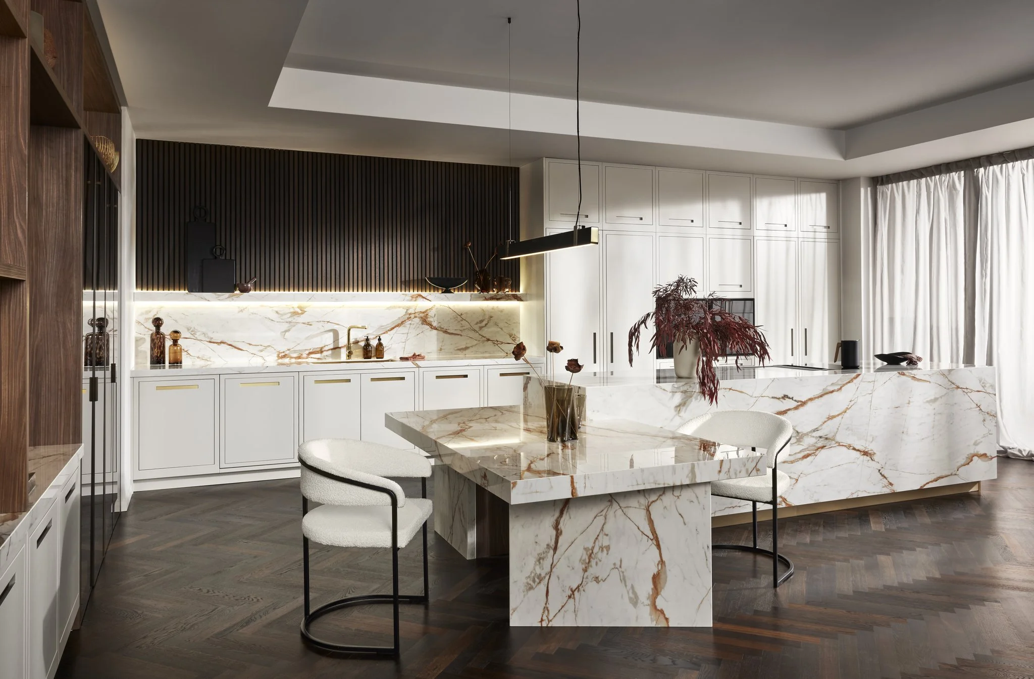 Modern kitchen with marble countertops, white cabinets, wooden elements, and contemporary furnishings.