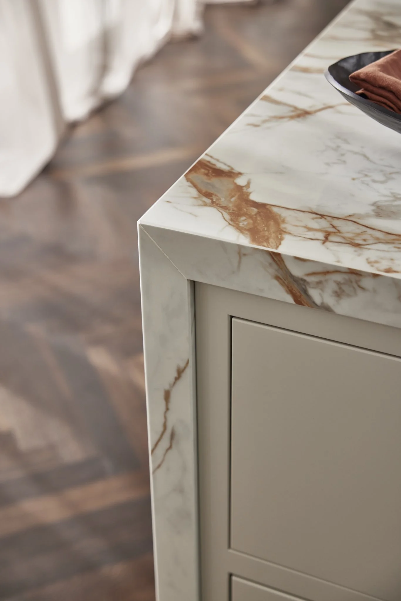 Close-up of a marble countertop with brown veining on a kitchen island, featuring modern cabinetry and a decorative tray.