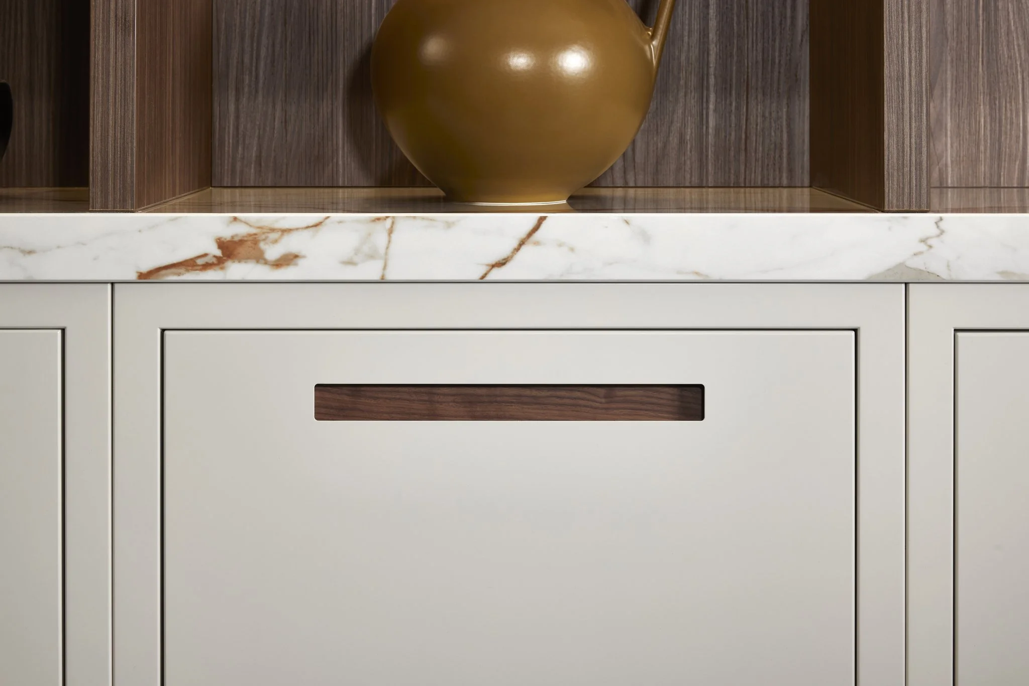 Modern style kitchen cabinet with a cut-out handle, marble countertop, and a brown ceramic vase.