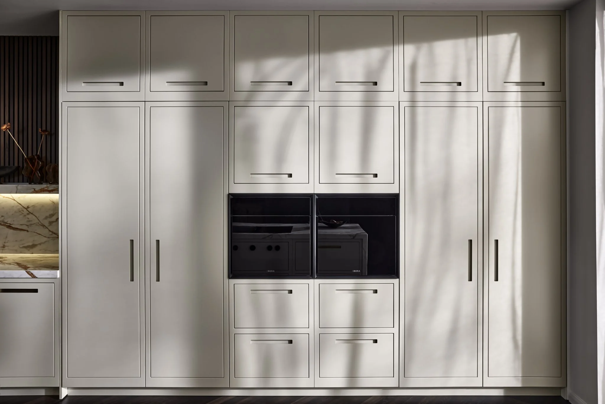 Modern kitchen cabinetry with built-in appliances and sleek handles, under soft natural lighting.