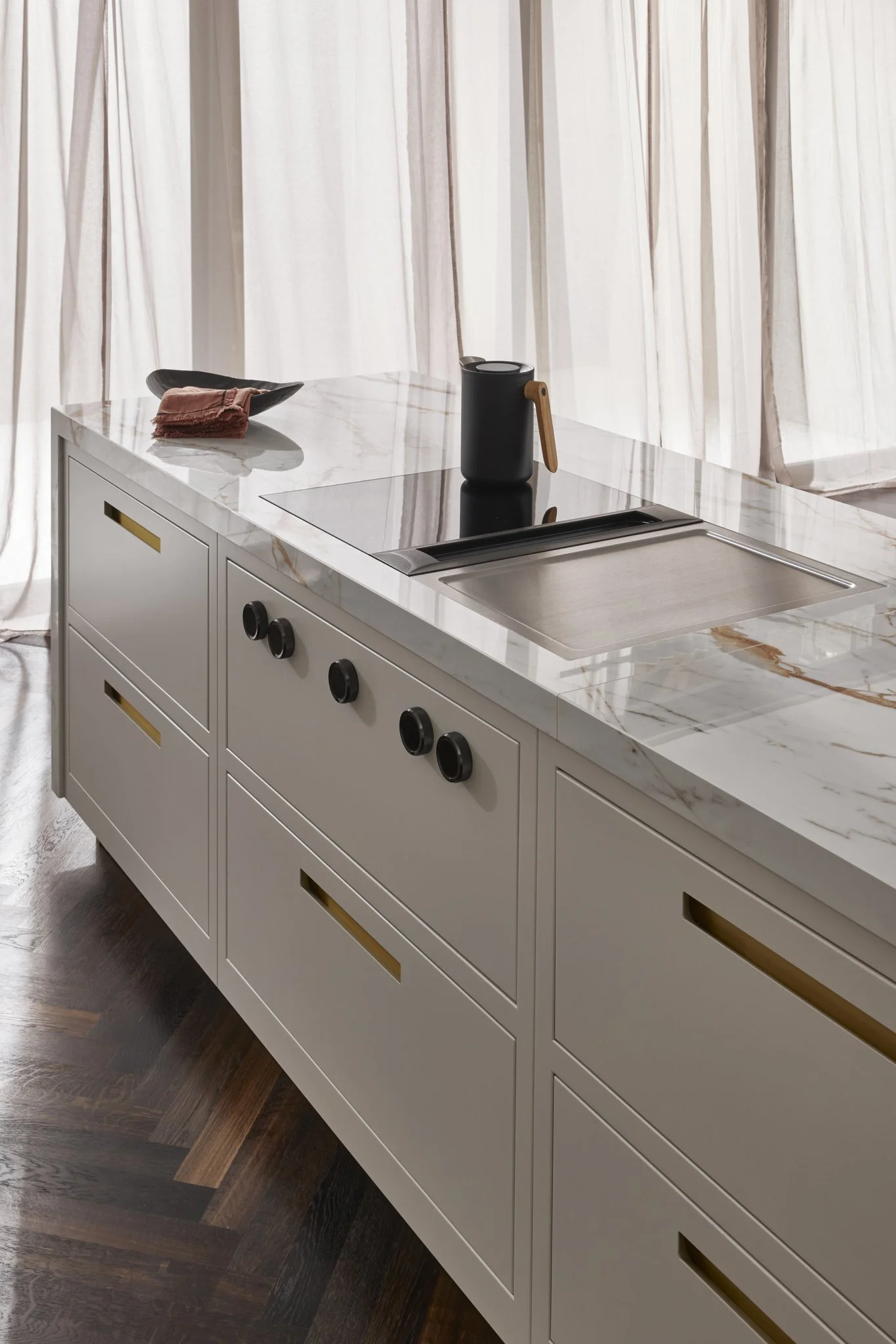 Modern kitchen island with marble countertop, induction cooktop, and black jug.