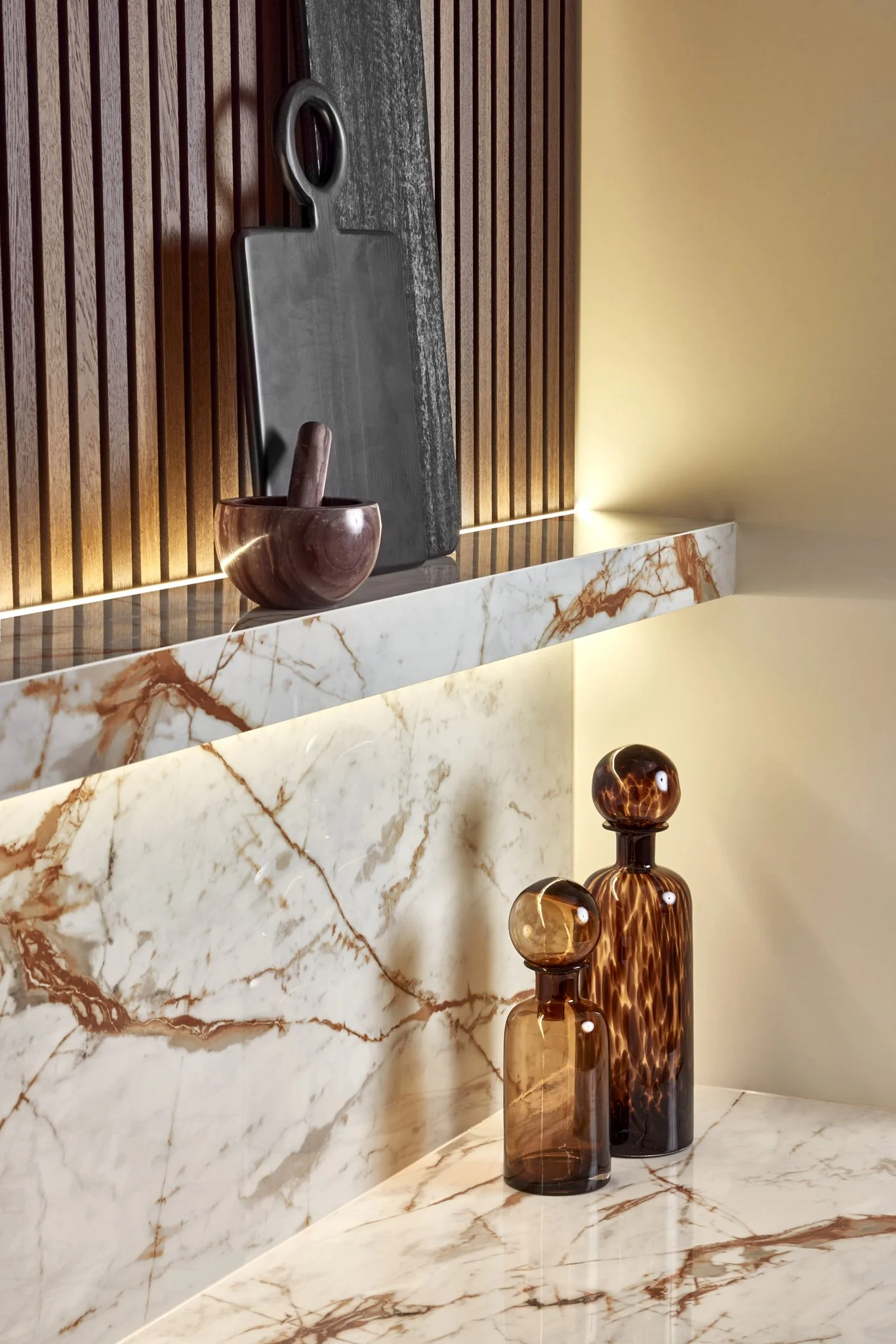 Marble countertop with decorative brown glass bottles, a black cutting board, and a wooden mortar and pestle.