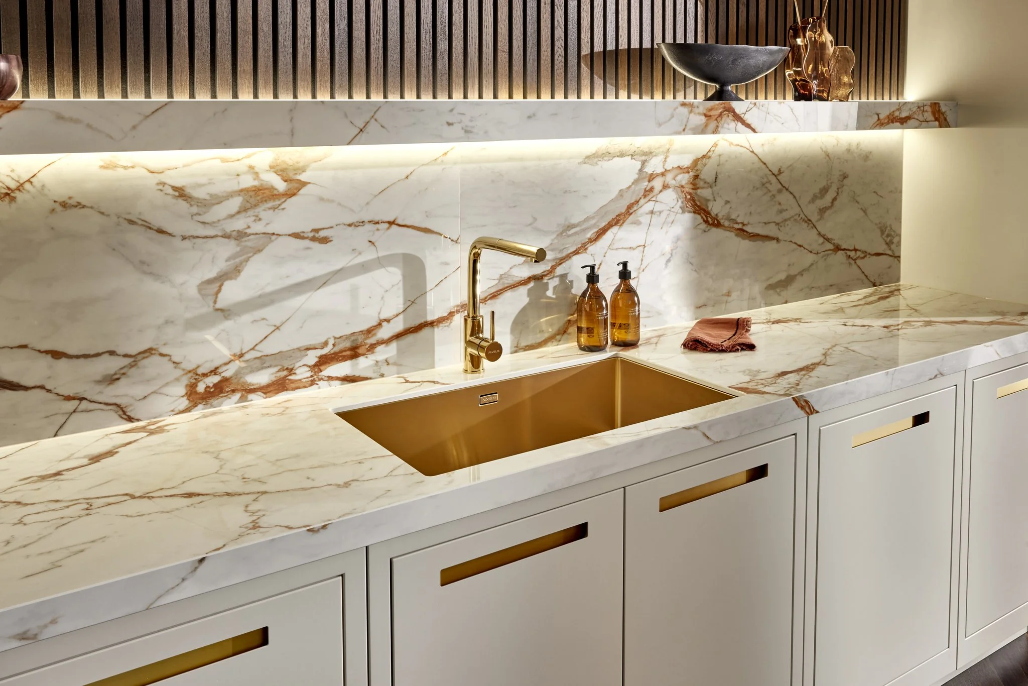 Modern kitchen with marble countertop, gold faucet, and decorative items.