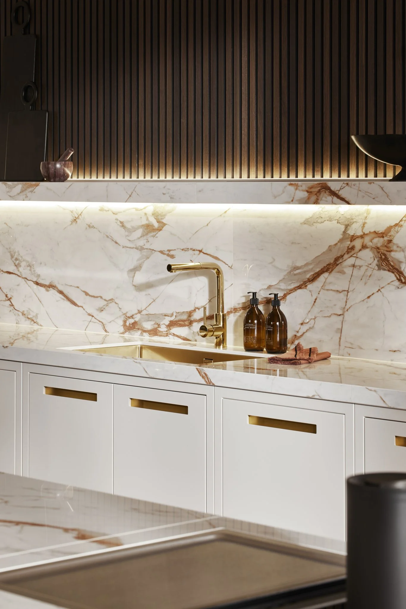 Modern kitchen with marble backsplash and countertop, gold faucet, and brown cabinetry