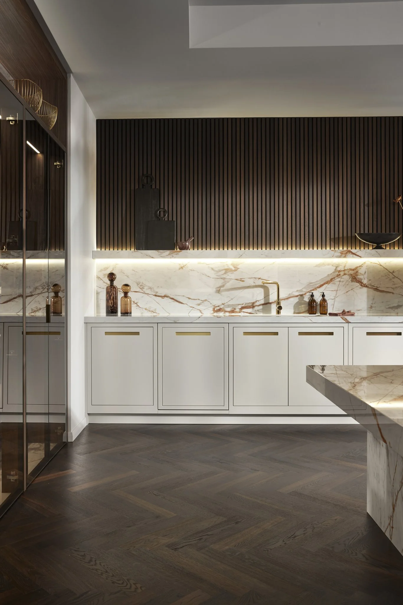 Modern kitchen interior with white cabinets, marble countertops, and backsplash, featuring dark wood accents and parquet flooring.