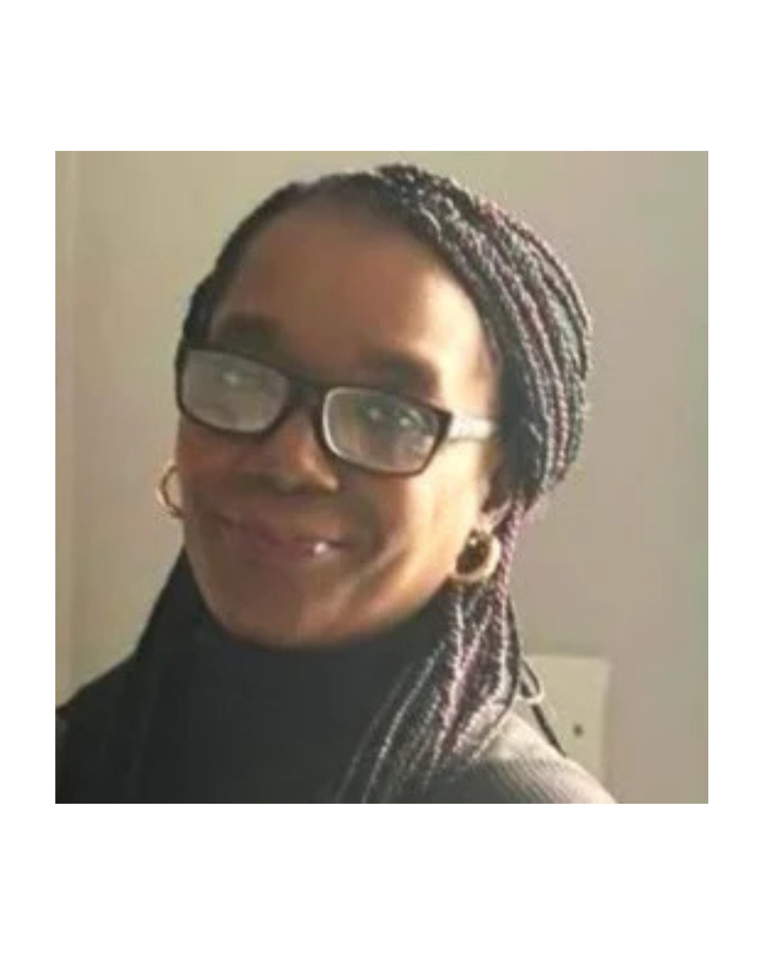 A female counsellor and CBT Therapist with braided hair, glasses, and hoop earrings smiling at the camera.