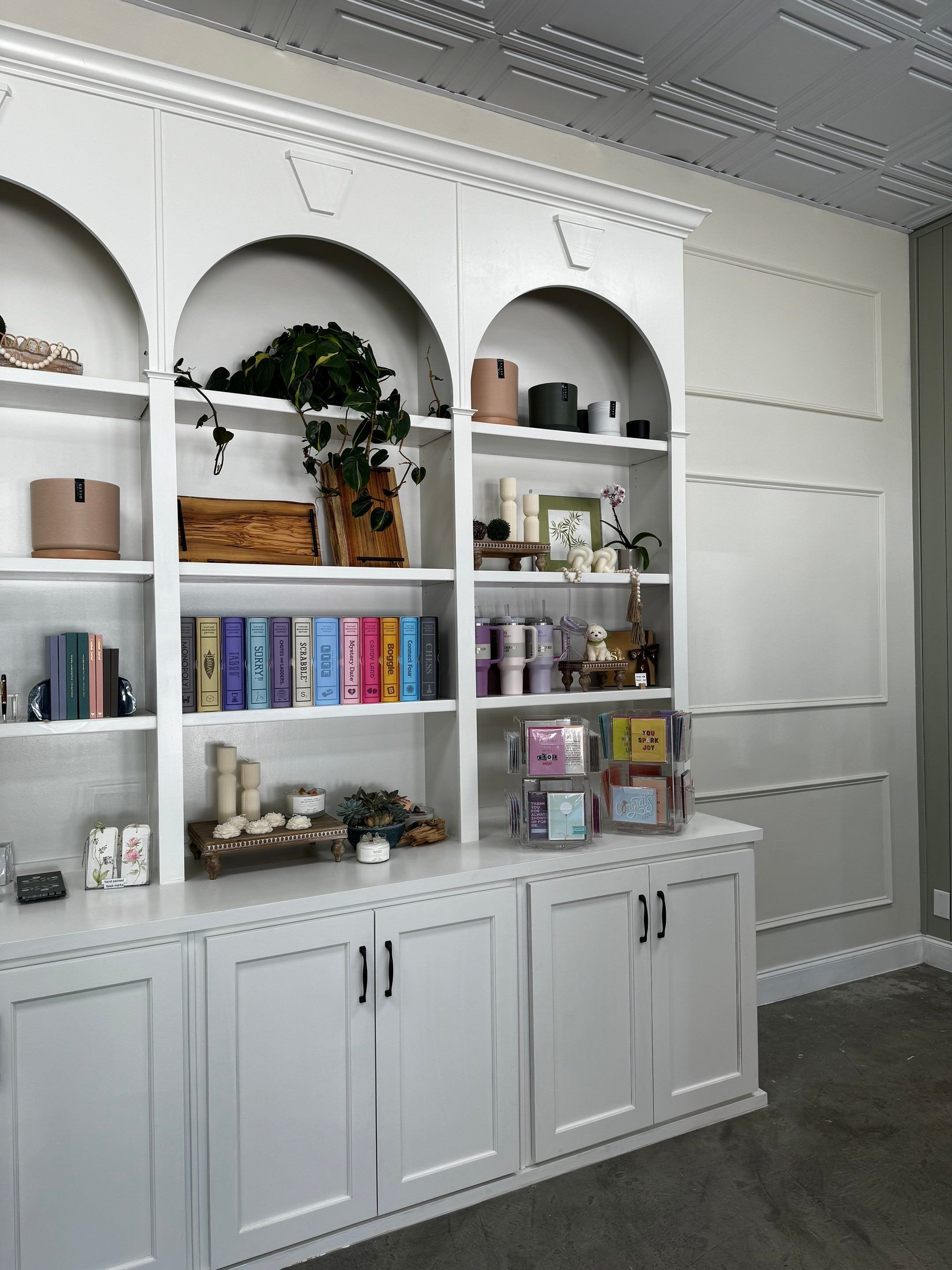 White built-in bookshelf with decorative items, books, plants, and storage containers, against a paneled wall, in a modern interior.