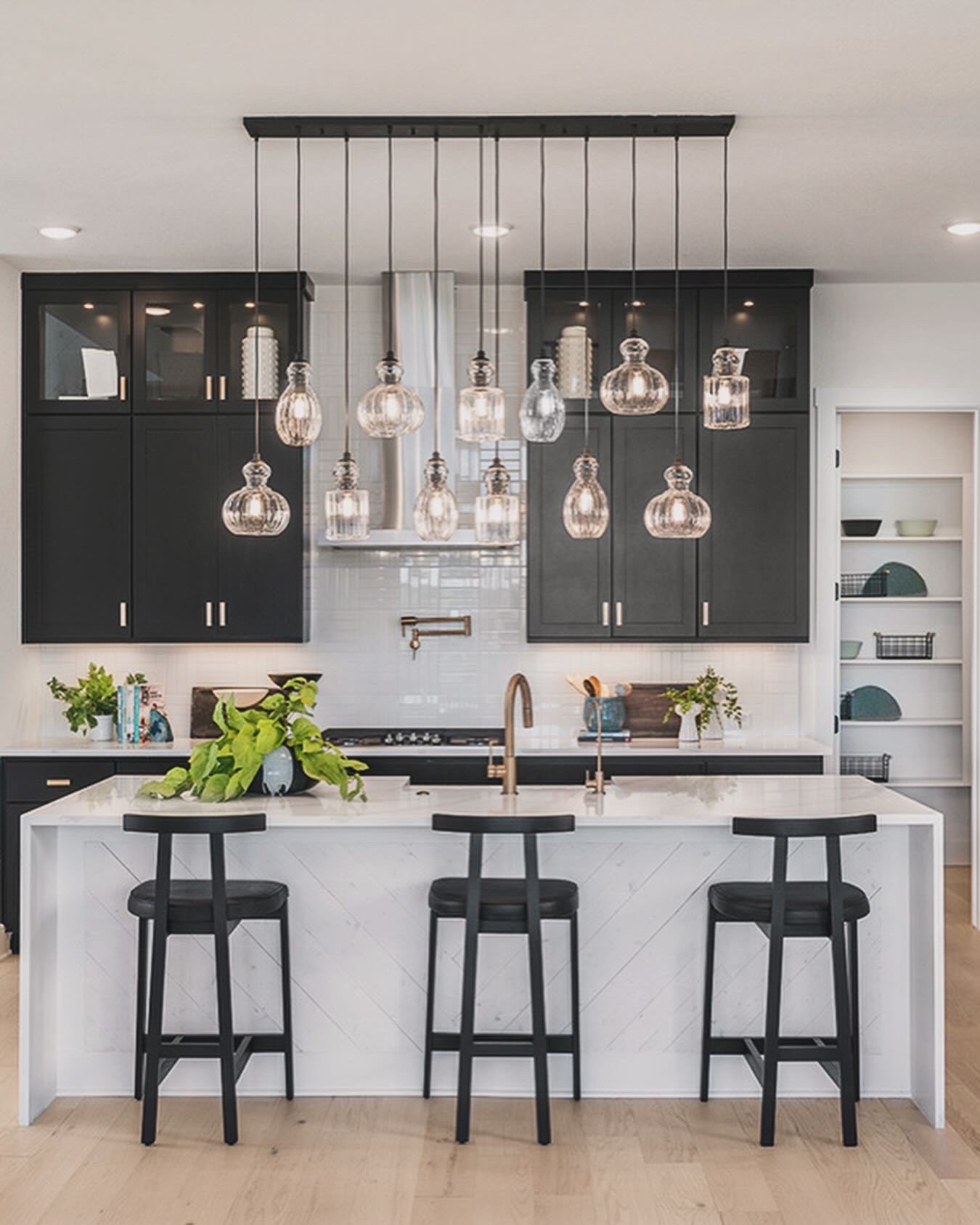 Modern kitchen with black cabinets, white marble island, hanging pendant lights, and open shelving.