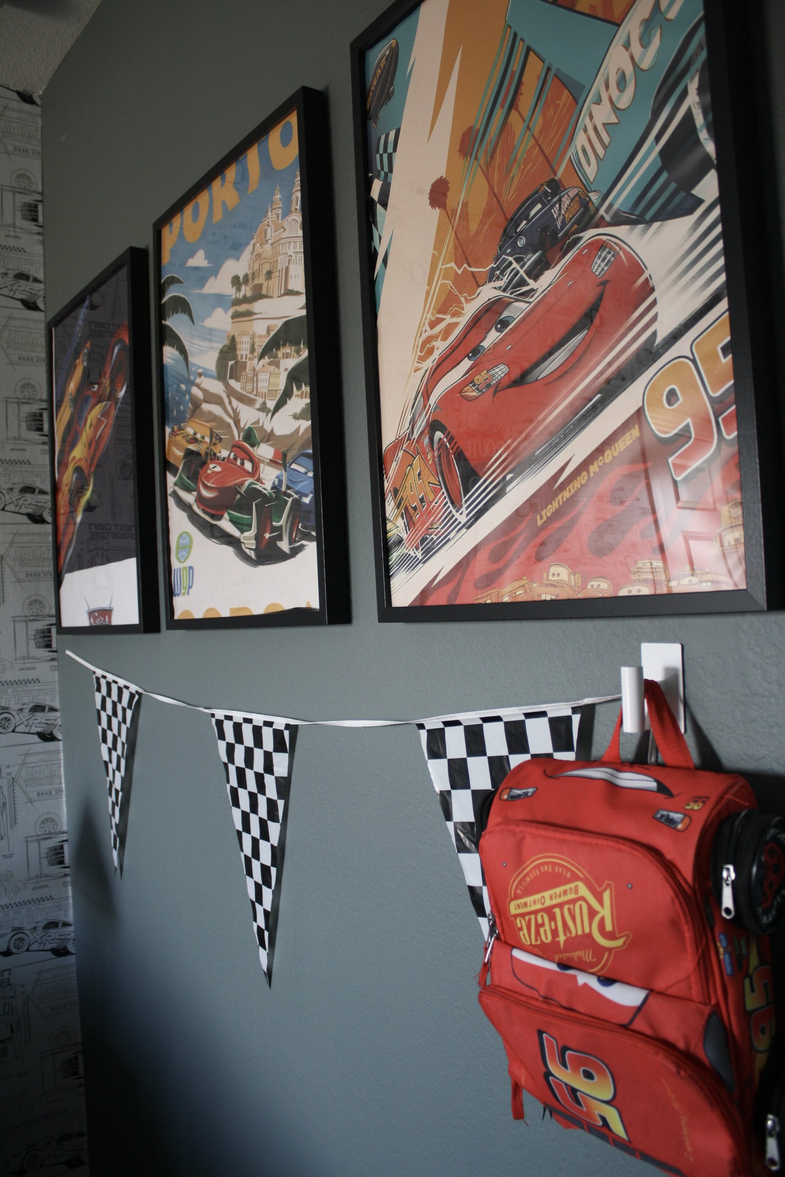 Wall decorated with framed 'Cars' animated movie posters, black and white checkered banners, and a red Lightning McQueen backpack.