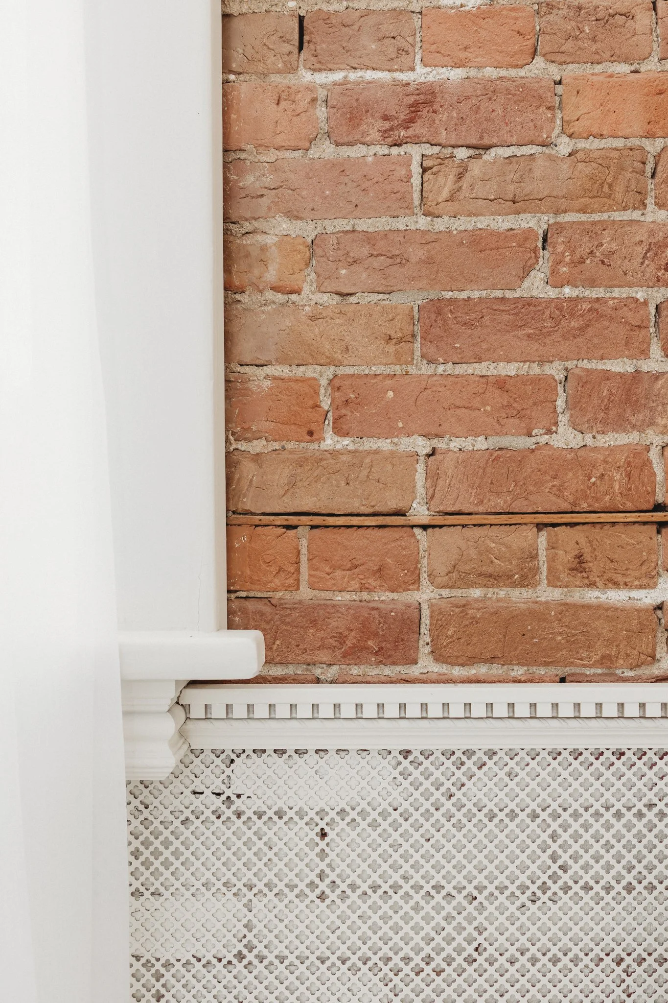 Close-up of a brick wall with a white corner of a building and white decorative molding near the bottom.