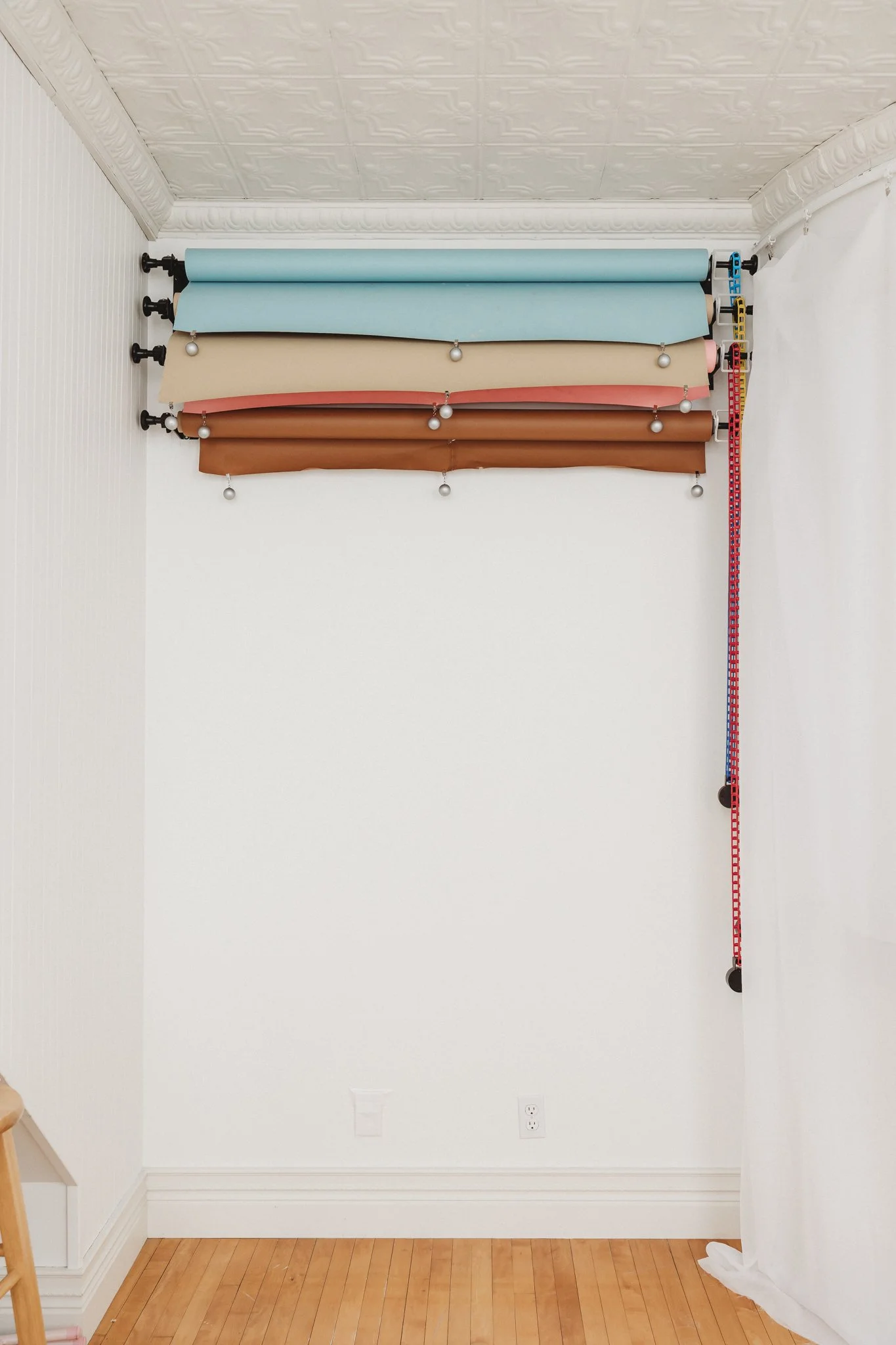 Four rolls of colored wrapping paper and some measuring tapes hanging on the wall.