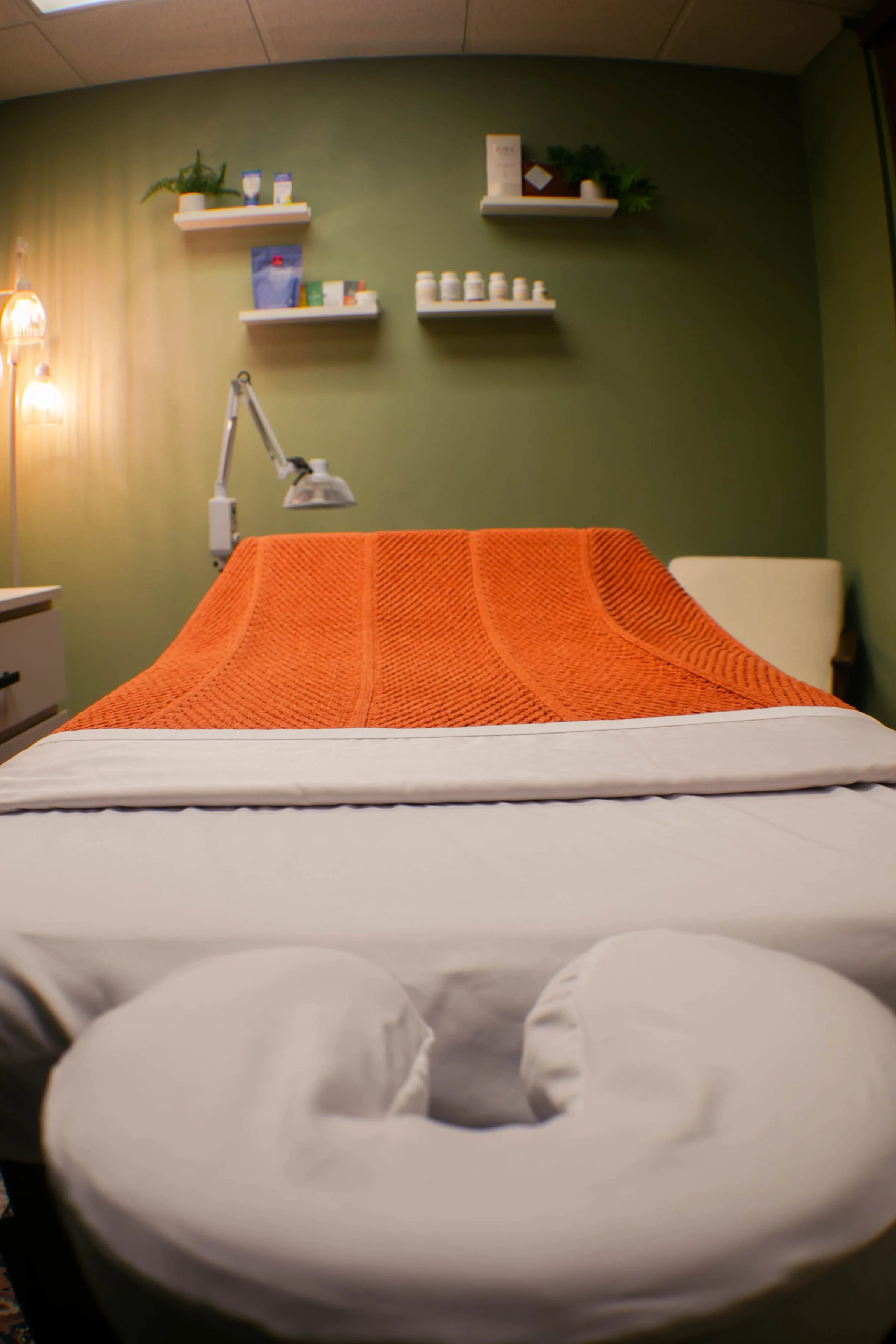 A massage or treatment bed with an orange towel in a room with green walls, shelves with various medicine bottles. Acupuncture. Kirkland, Washington. Vancouver, Washington. Mental health. Women's health. Fertility. Menopause. Microneedling. Cosmetic