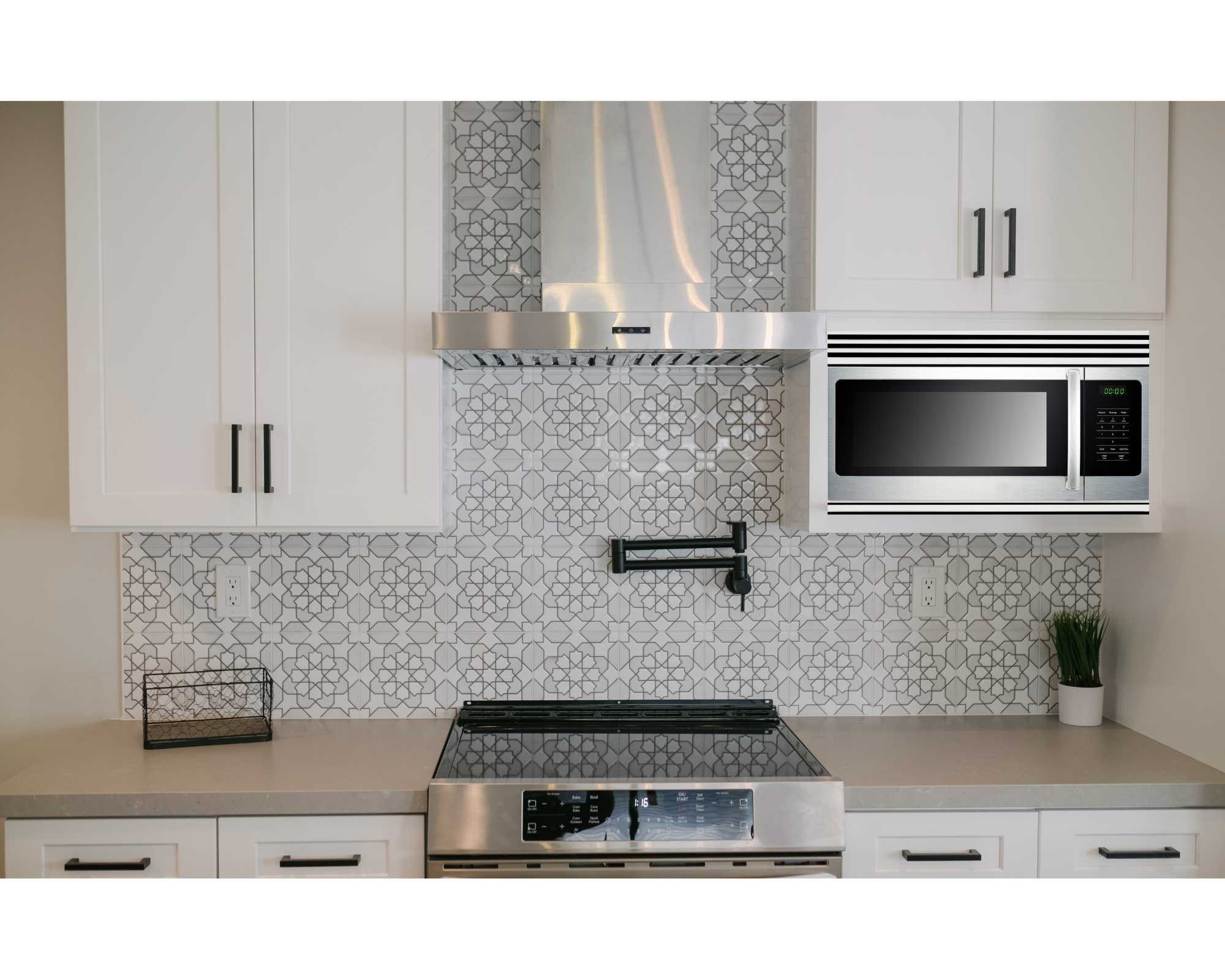 Modern kitchen with white cabinets, stainless steel microwave, stove, and vent hood, patterned backsplash, small plant, and a black wire basket.