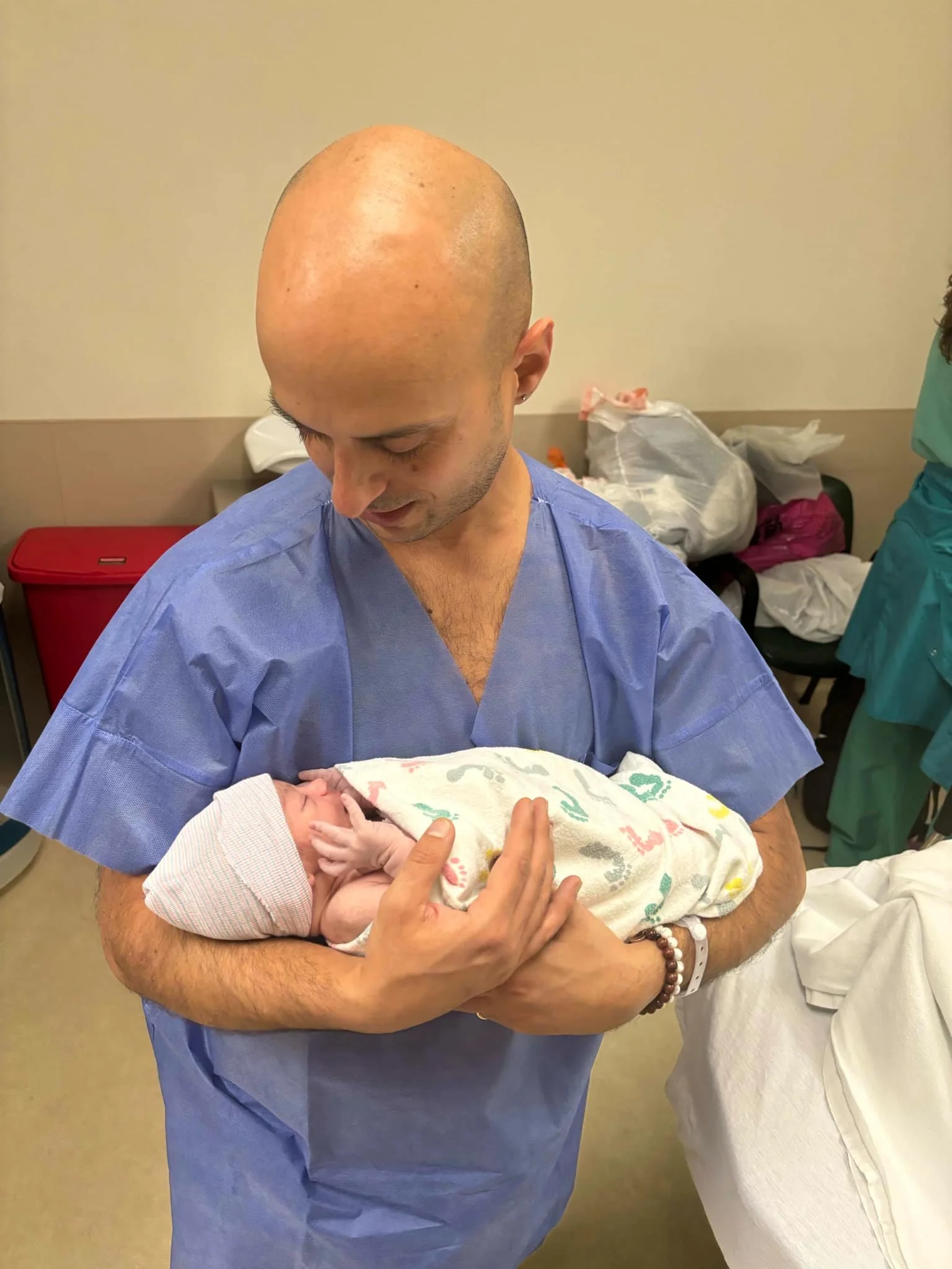 Man in blue hospital gown holding newborn baby wrapped in blanket.
