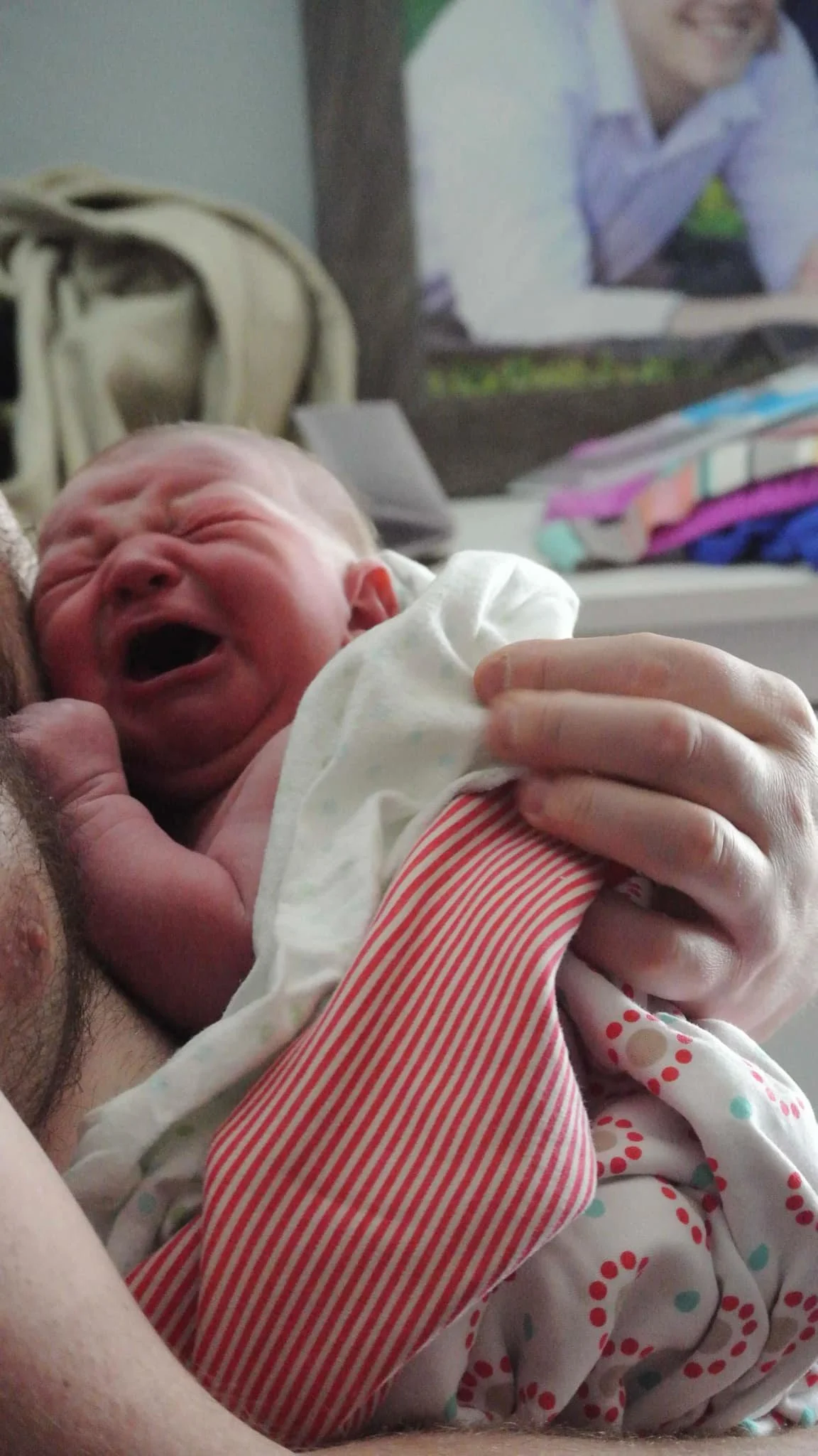 Crying newborn wrapped in blanket, held by a person's hands.