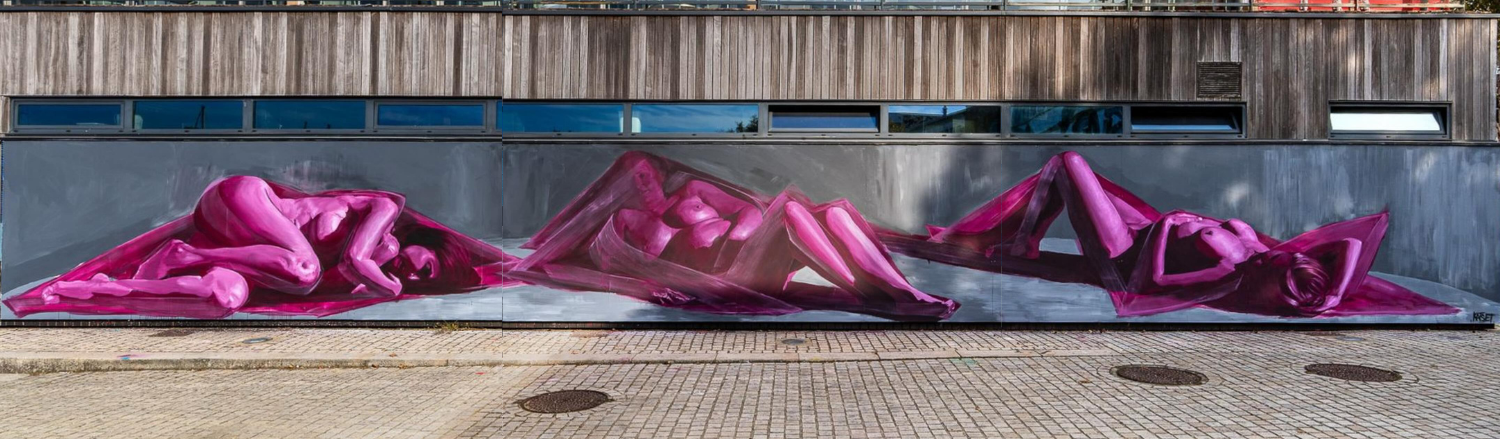 Une fresque murale abstraite peinte sur un bâtiment en bois, représentant plusieurs figures humaines stylisées et colorées.