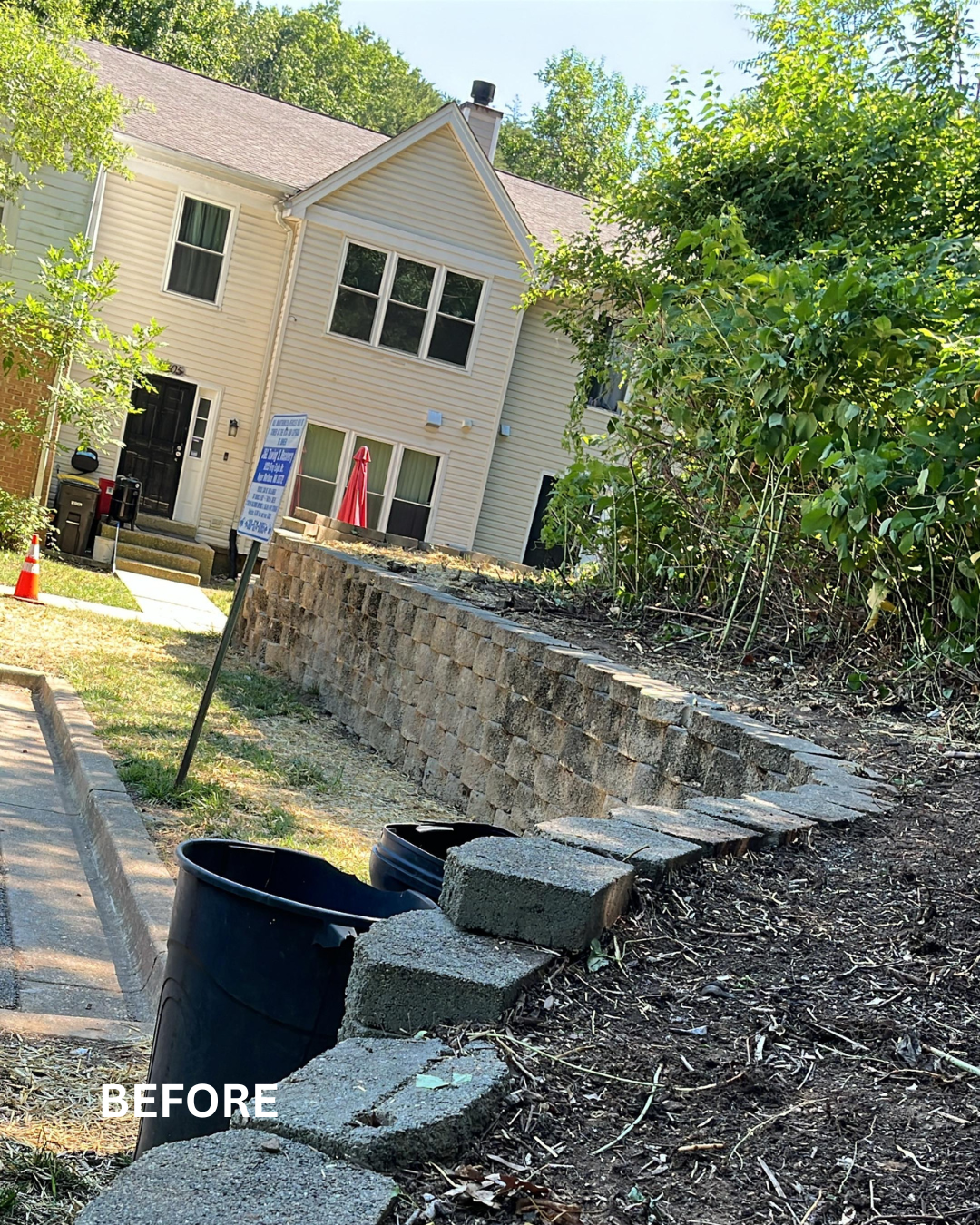 A residential front yard with a brick retaining wall under construction, partially completed, with landscaping and a house in the background.