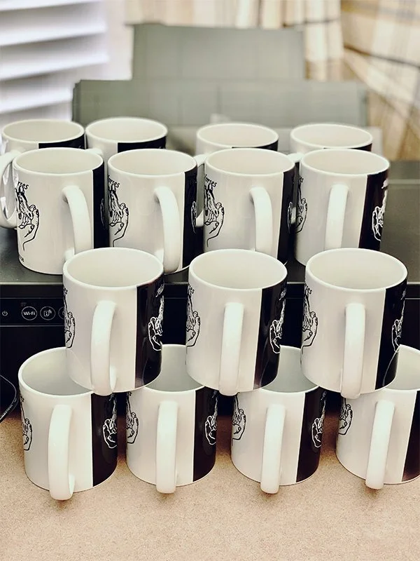 Stacked white ceramic mugs printed with a company logo on it.