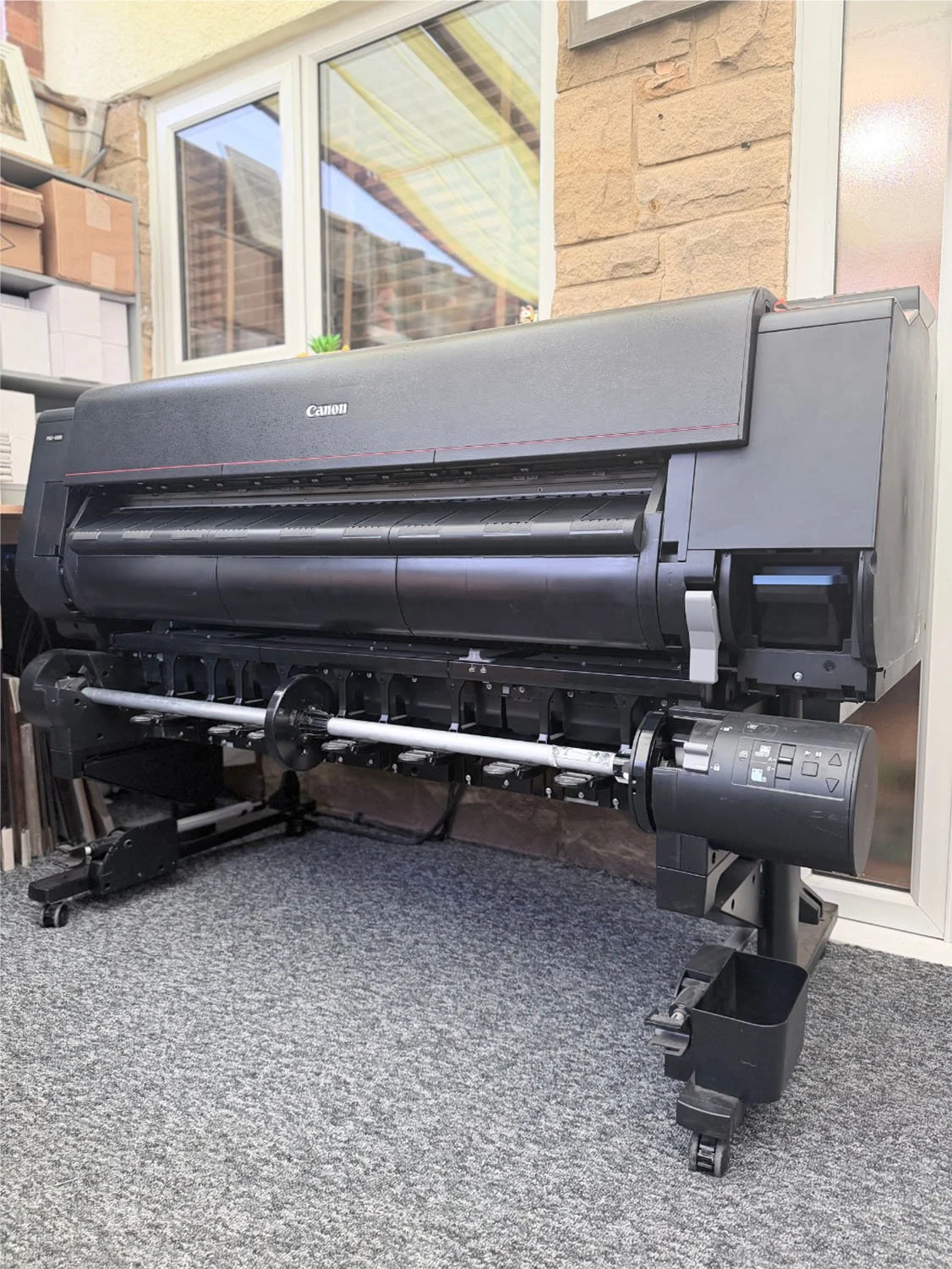 Large, black and gray Canon large-format printer on a carpeted floor situated in an office.