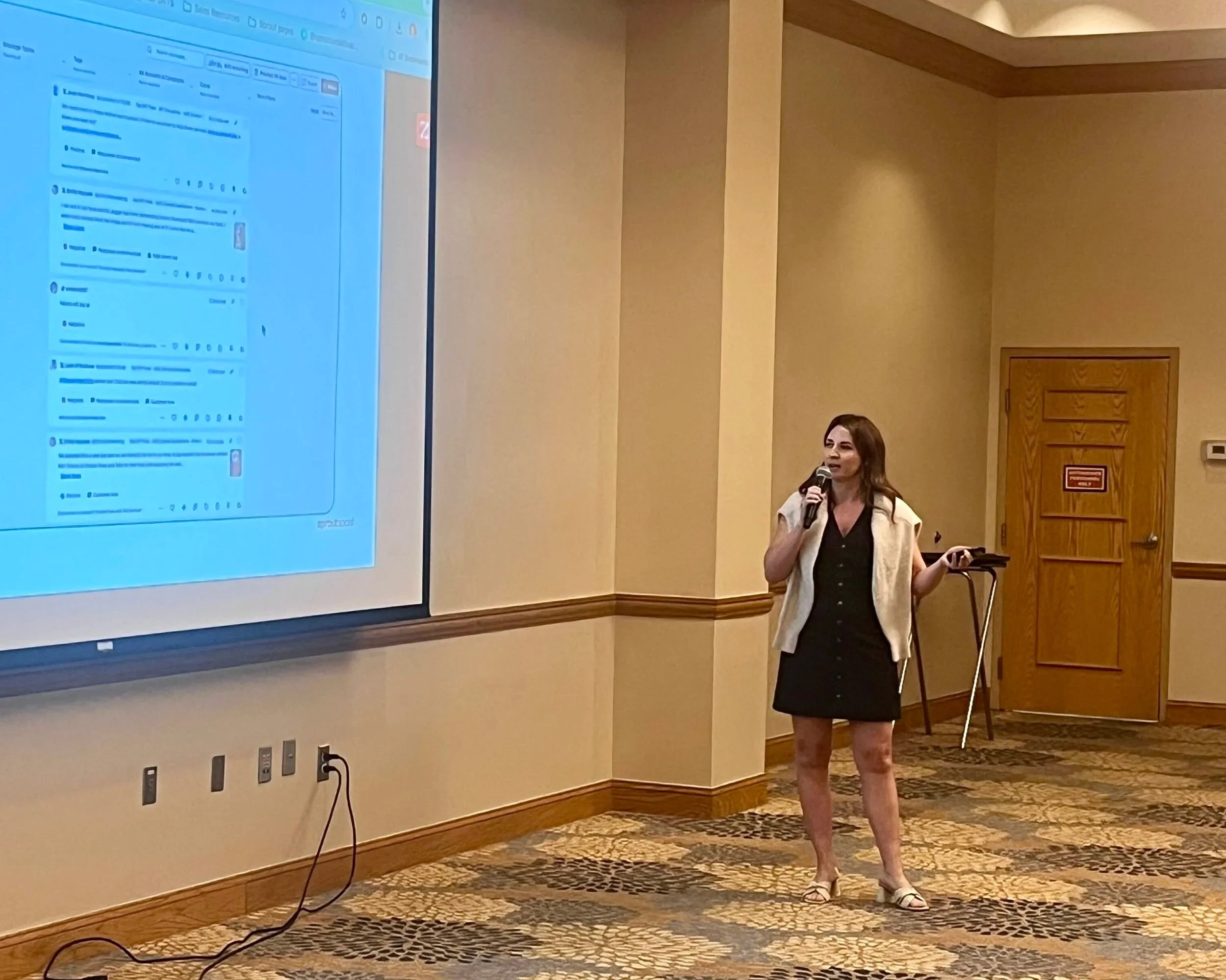 Woman giving a presentation in a conference room with a large screen displaying a social media page.