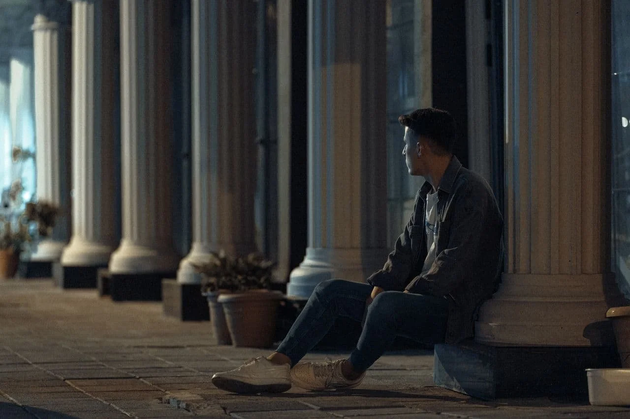 man-in-jacket-and-jeans-sitting-on-pillar