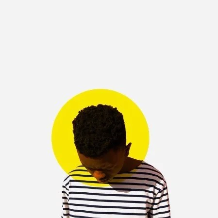 A boy with short curly hair looking downward, wearing a striped shirt, with a yellow circle behind his head on a white background.