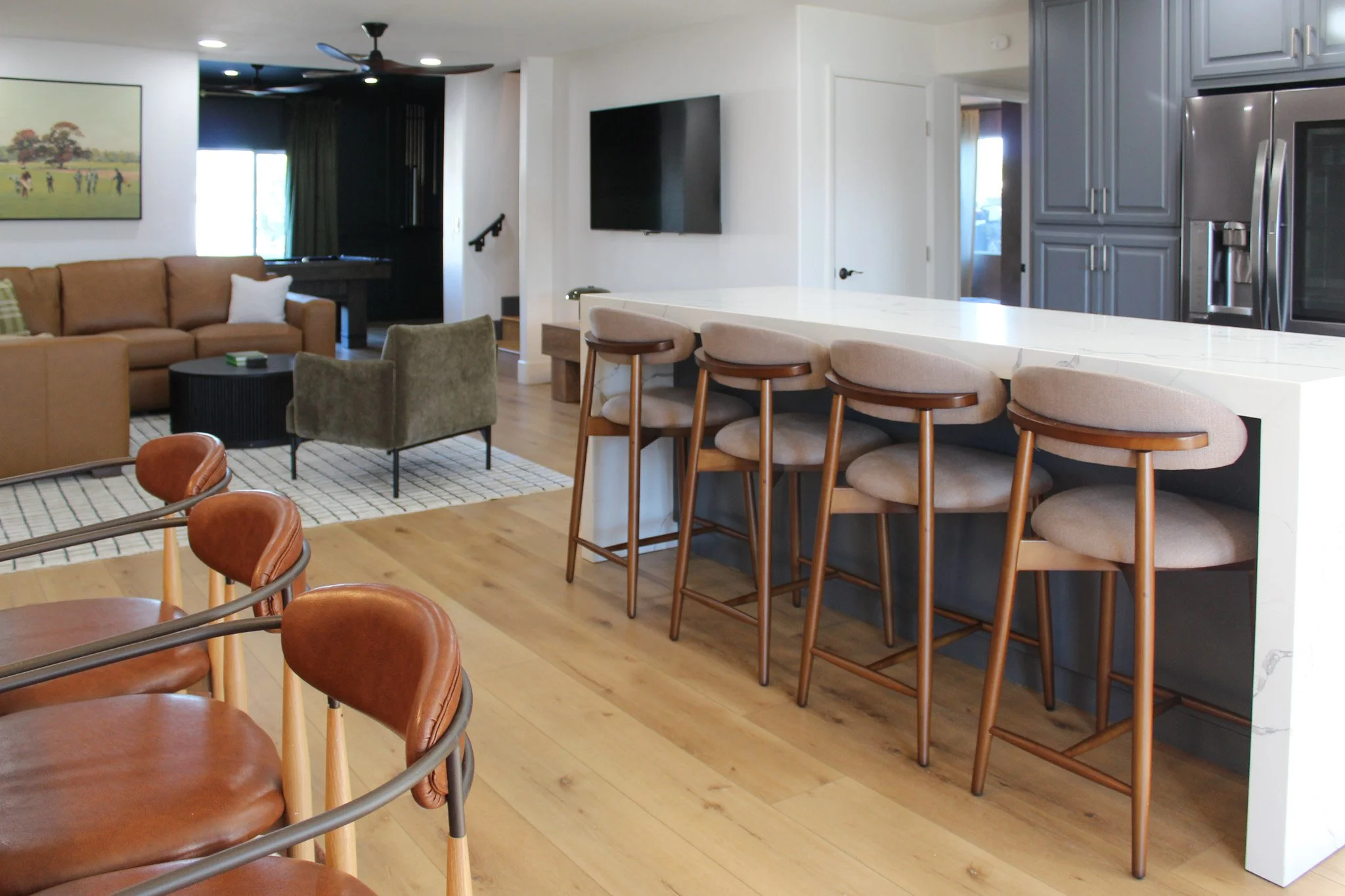 Open-concept living room and kitchen with bar stools, a beige sofa, green armchair, and flat-screen TV.