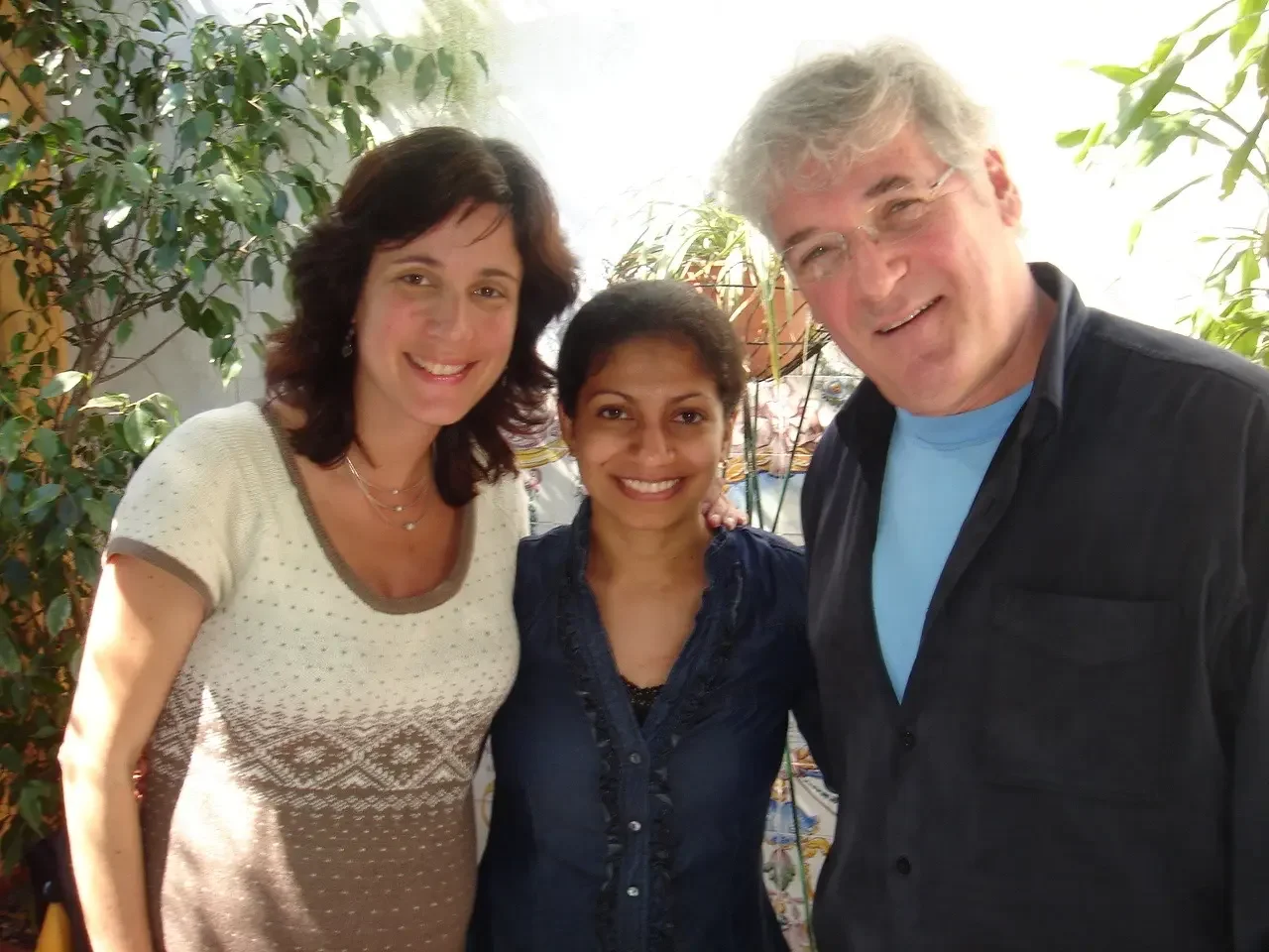 Three people smiling and posing together indoors with plants in the background.