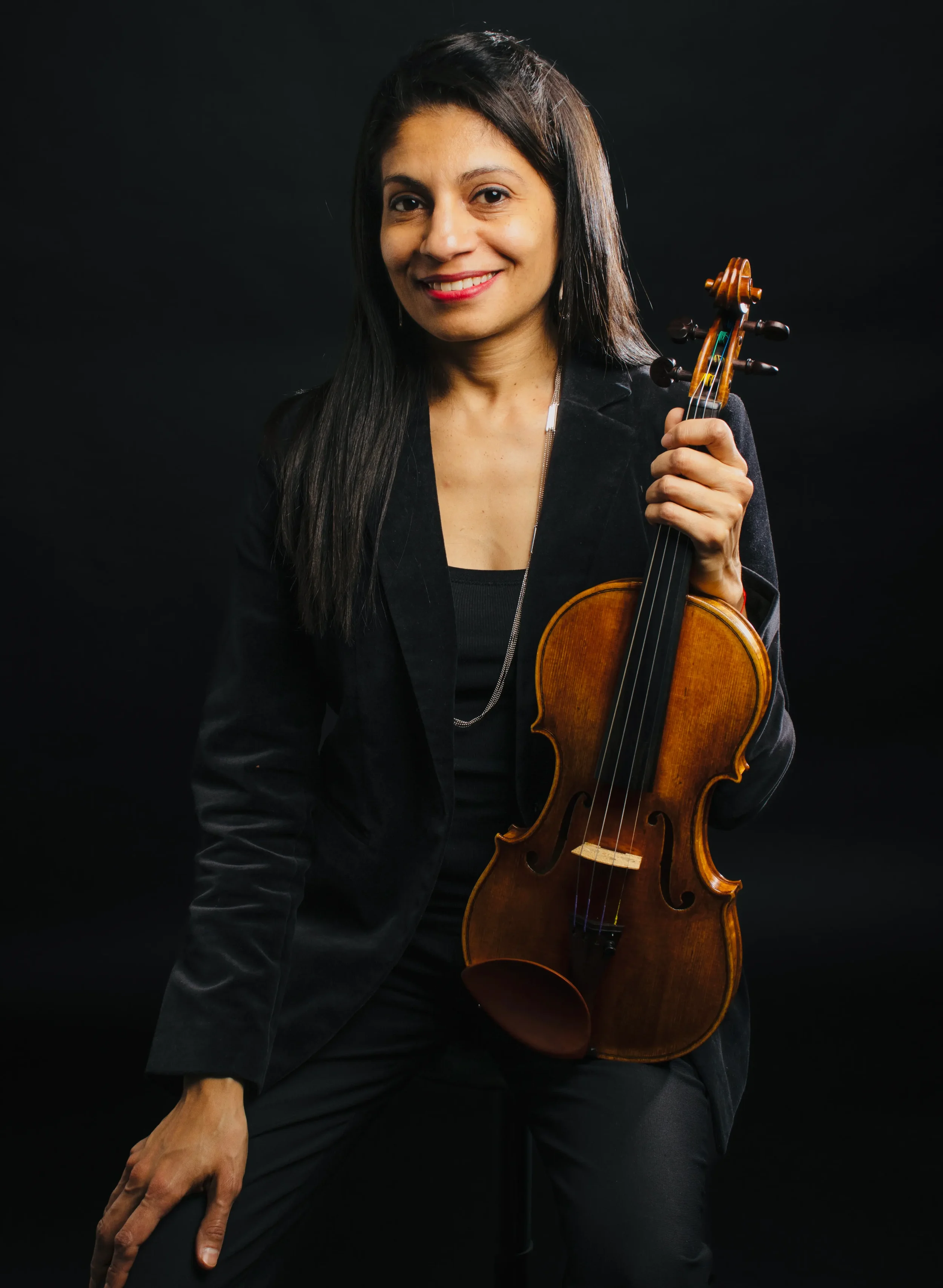 Women holding a violin, dressed in black against a dark background.