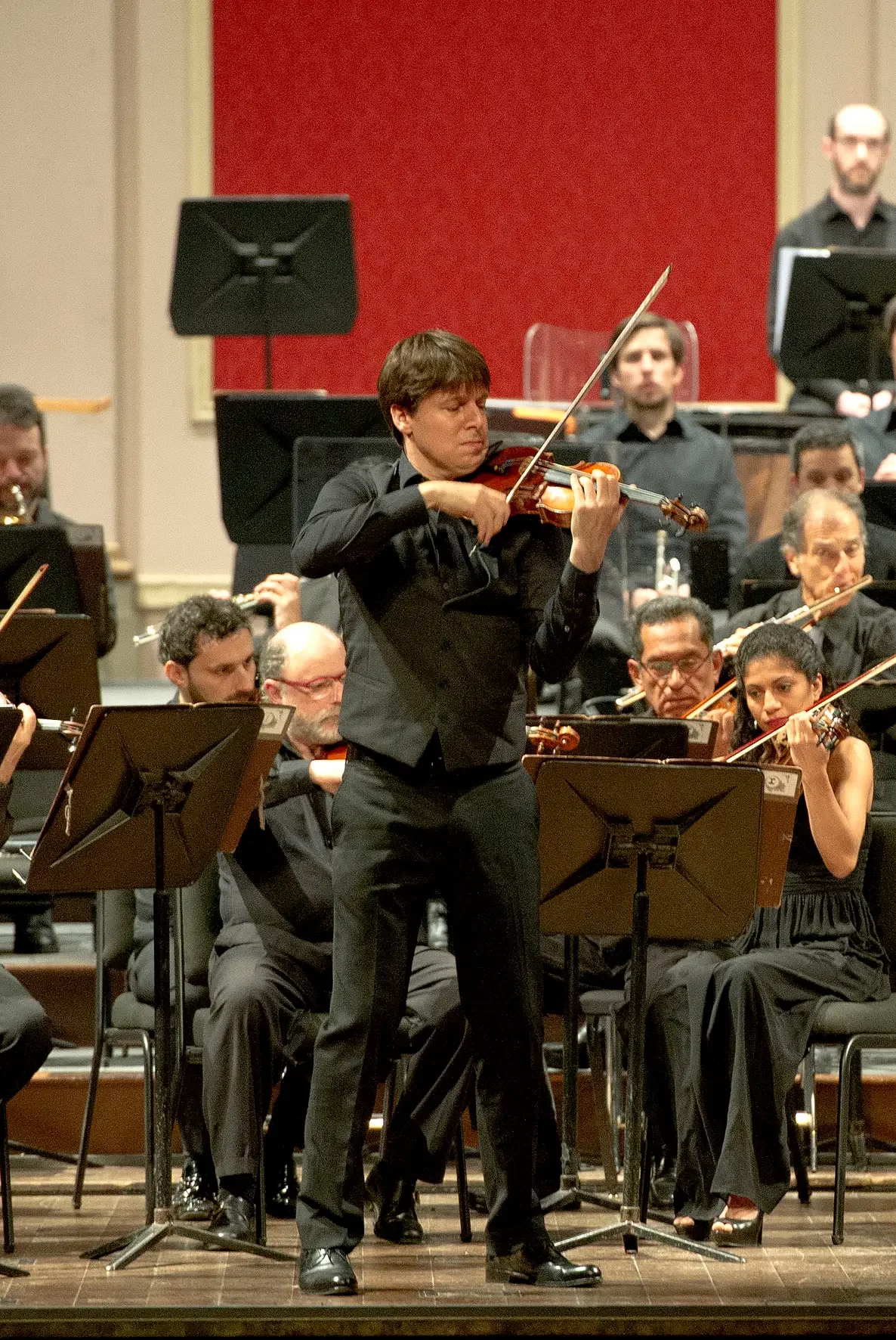 Orchestra conductor playing violin on stage during a concert.