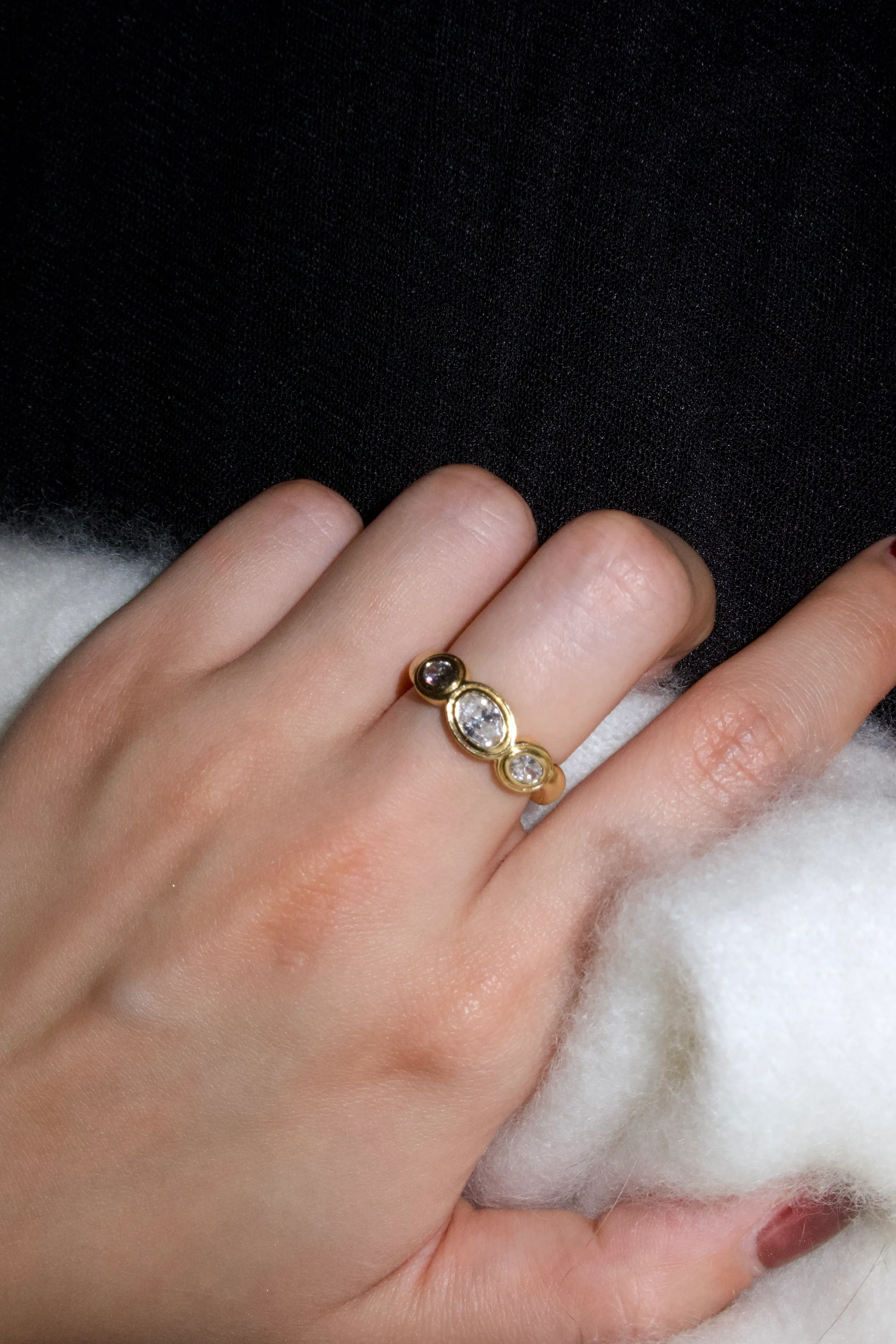 Close-up of a hand wearing a gold ring with multiple diamonds, resting on white fluffy material.