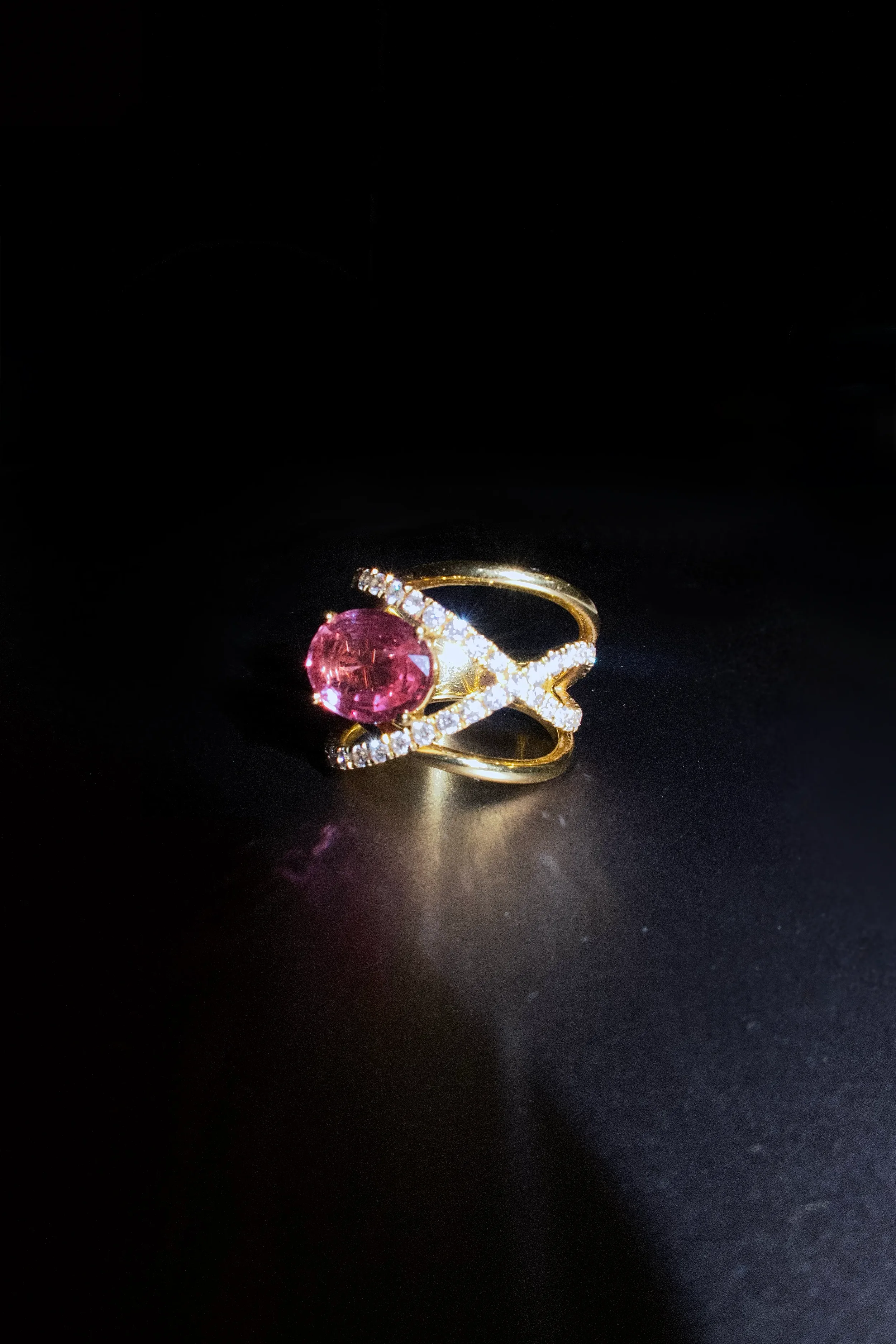 Gold ring with pink gemstone and diamond accents on a black background.