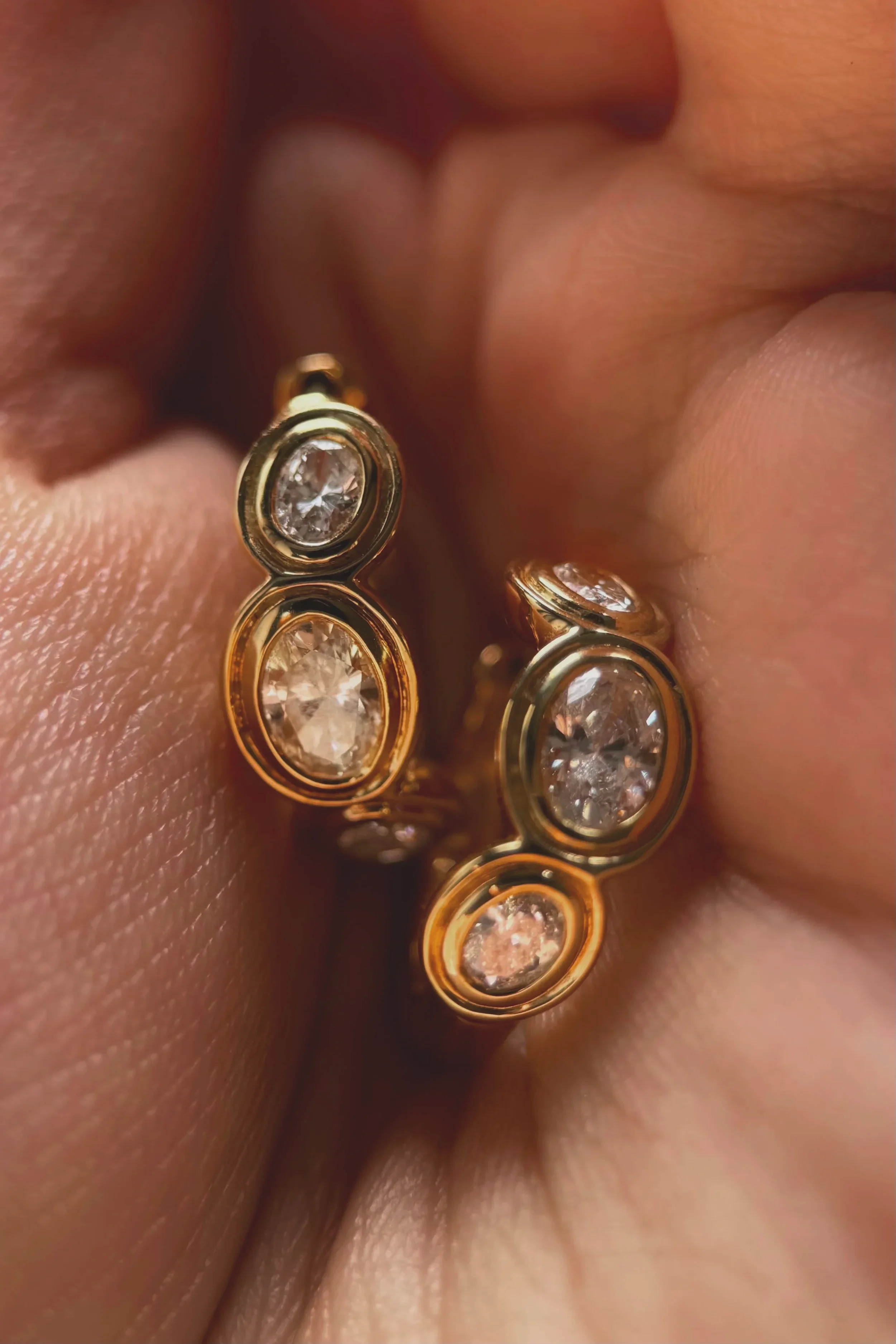 Close-up of a person's ear adorned with multiple gold and silver earrings featuring clear gemstones.