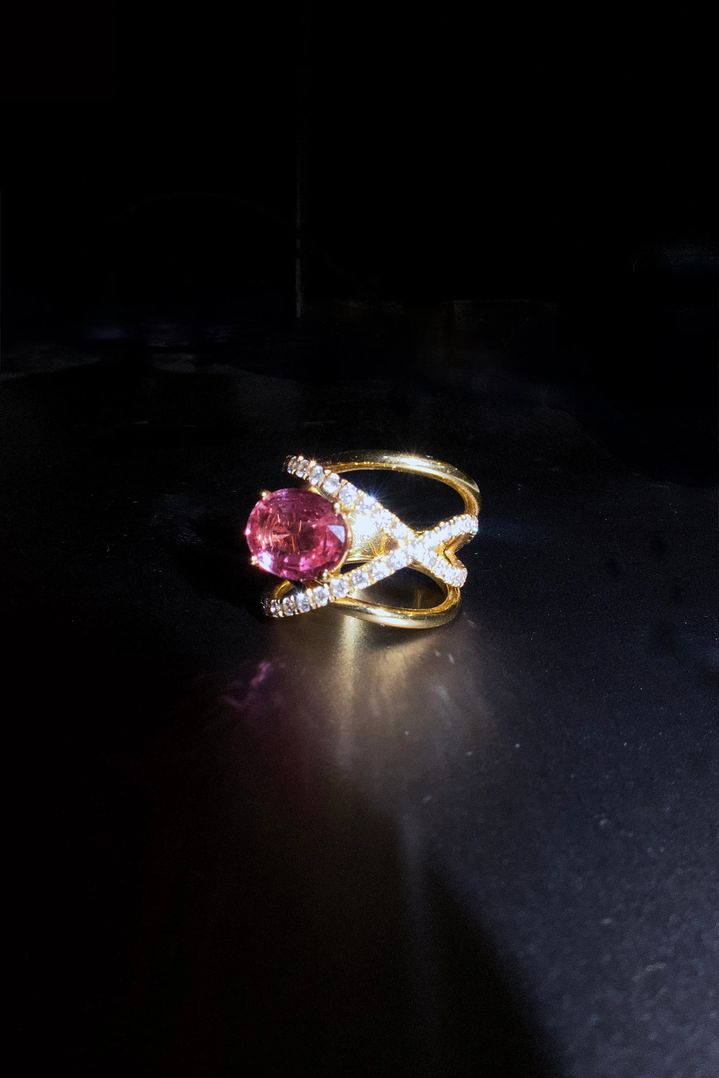Gold ring with a pink gemstone and small diamonds, on a black surface.