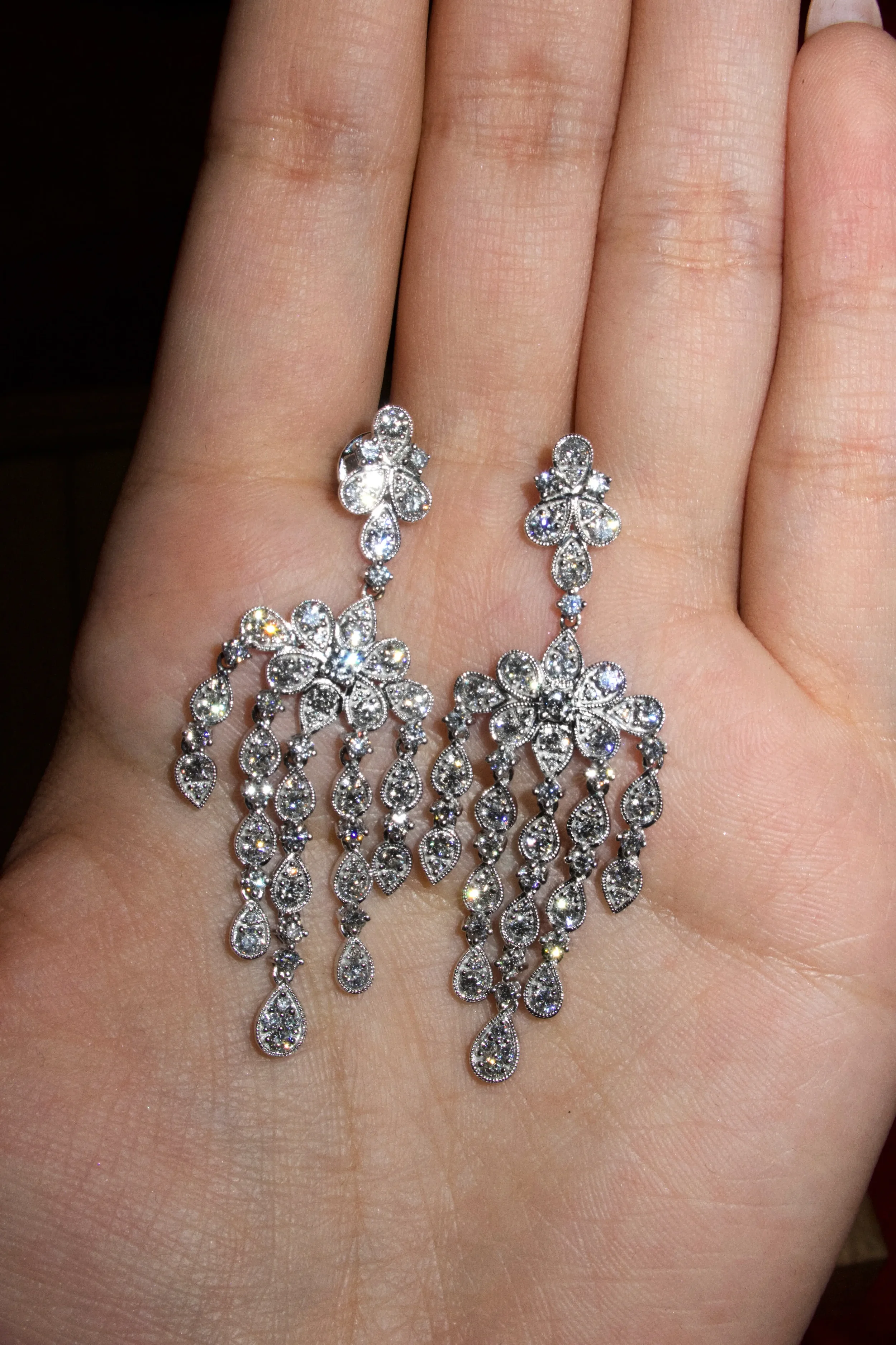 Silver chandelier earrings with floral and teardrop-shaped gemstones being worn on a person's hand.