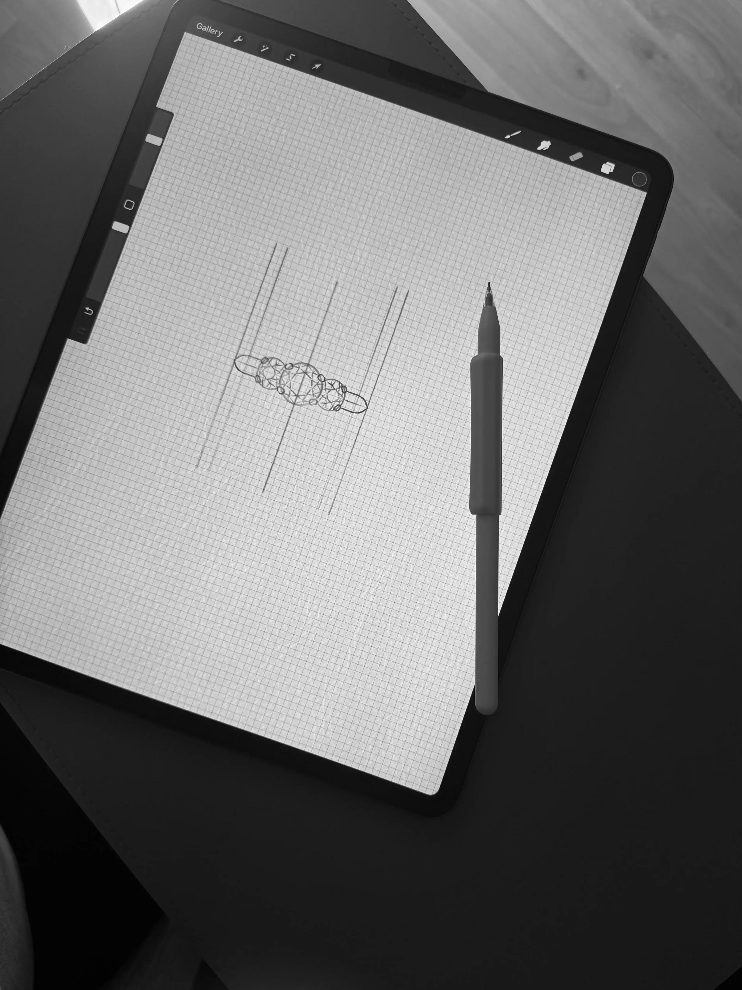 A digital drawing tablet with a grid screen displaying a wireframe sketch of a pendant with beads and a spherical centerpiece, along with a stylus resting on the screen.
