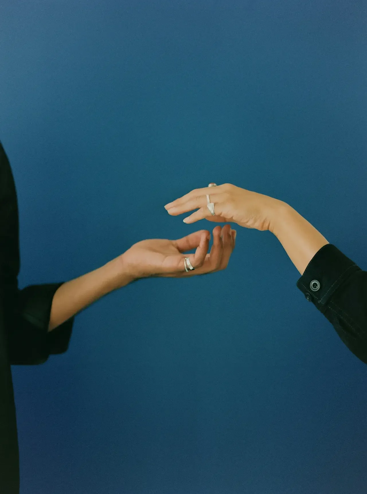 Two hands with rings reaching toward each other against a blue background.