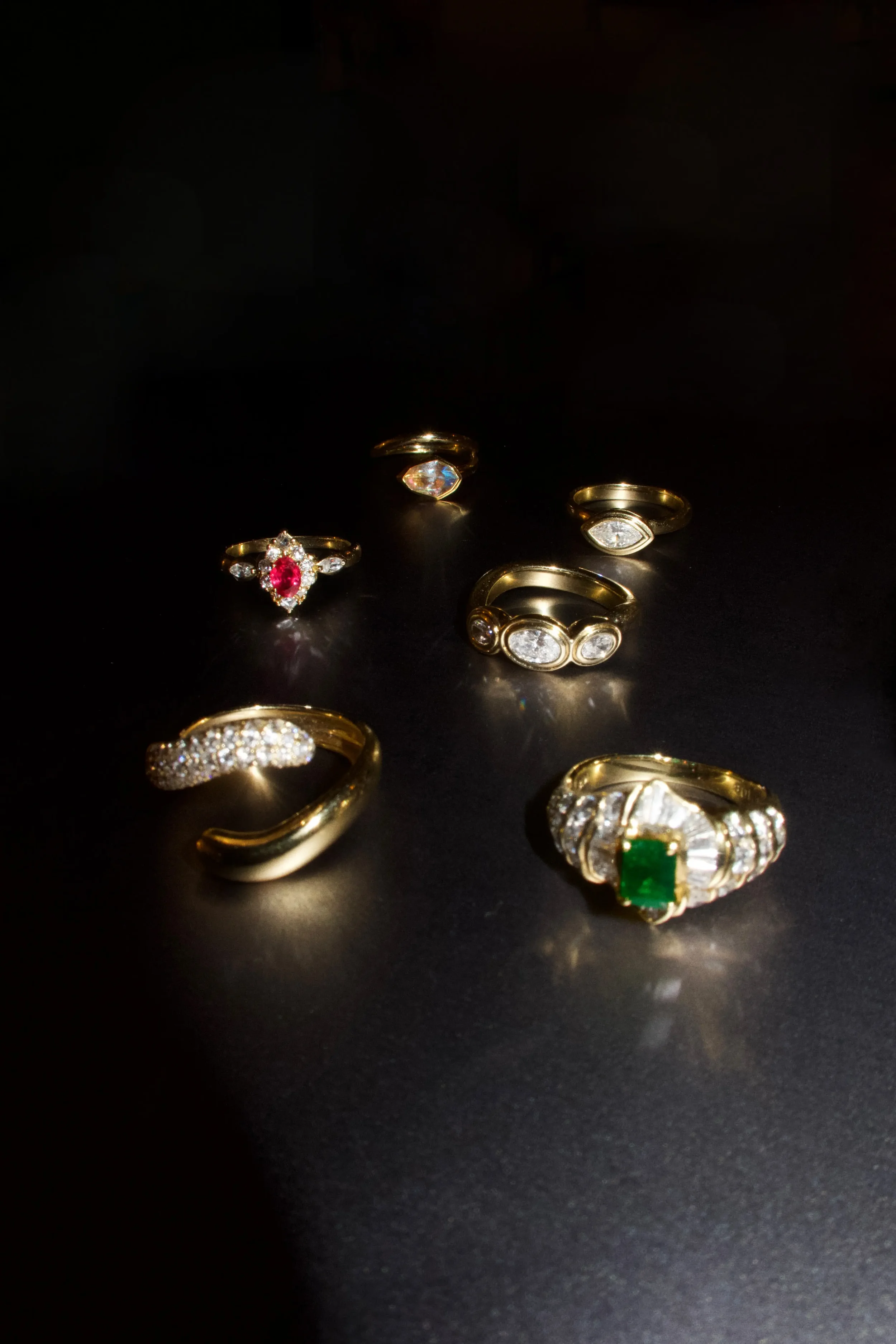 Several gold rings with various gemstones displayed on a dark surface.